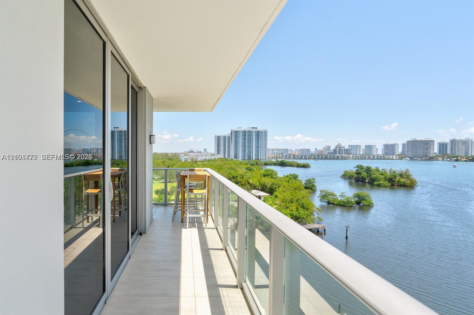 Covered terrace with tile flooring and a glass panel railing, featuring expansive water and skyline scenery