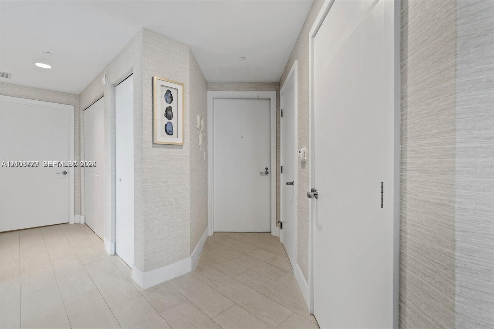 Entryway featuring neutral-toned textured wall covering, large-format tile flooring, multiple interior doors with brushed metal hardware, and recessed ceiling lighting
