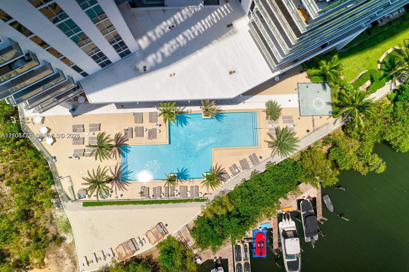 Aerial perspective featuring a swimming pool, paved sundeck, tropical landscaping, and private boat slips along the shoreline