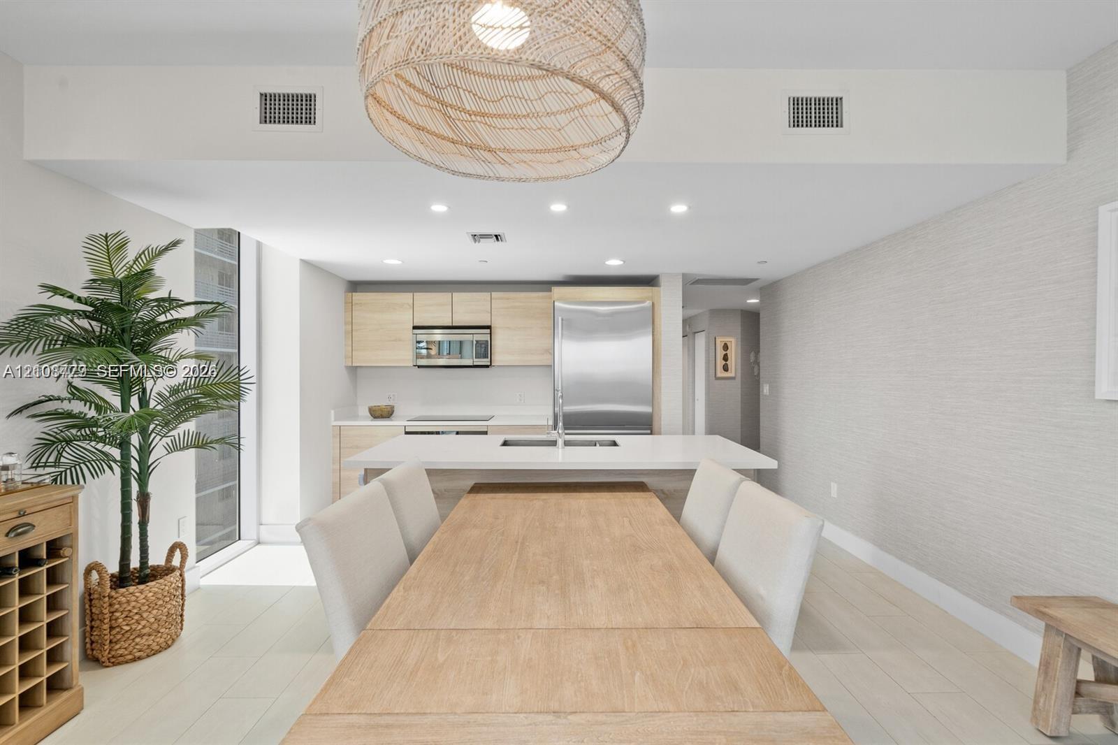 Kitchen featuring light wood-finish cabinetry, stainless steel appliances, a central island with a solid-surface countertop, recessed ceiling lighting, and woven pendant lighting Kitchen featuring light wood-finish cabinetry, stainless steel appliances, a central island with a solid-surface countertop, recessed ceiling lighting, and woven pendant lighting