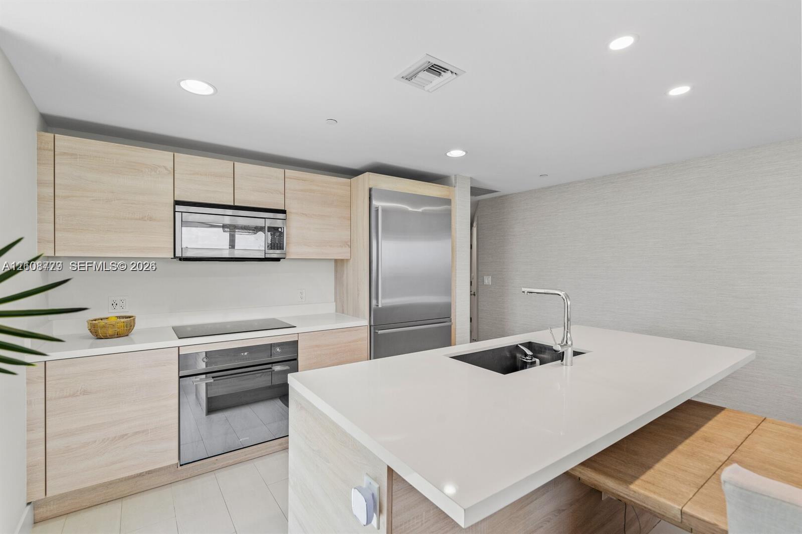 Kitchen featuring light wood-finish cabinetry, quartz countertops, a central island with an undermount sink and chrome faucet, recessed lighting, and stainless-steel appliances Kitchen featuring light wood-finish cabinetry, quartz countertops, a central island with an undermount sink and chrome faucet, recessed lighting, and stainless-steel appliances