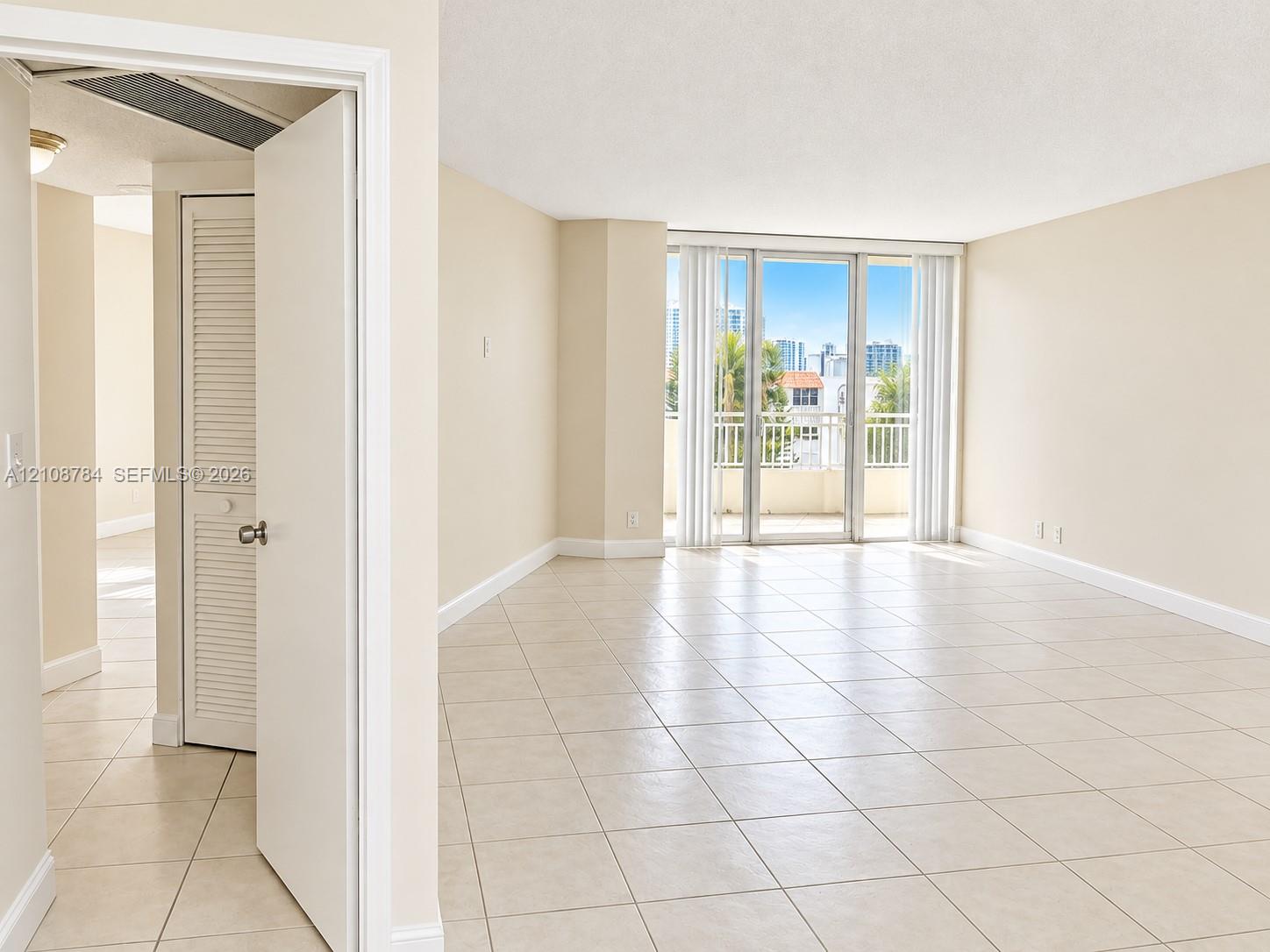 Open-concept room featuring light-colored ceramic tile flooring, floor-to-ceiling glass sliding doors, a metal-railed balcony, and louvered bifold closet doors