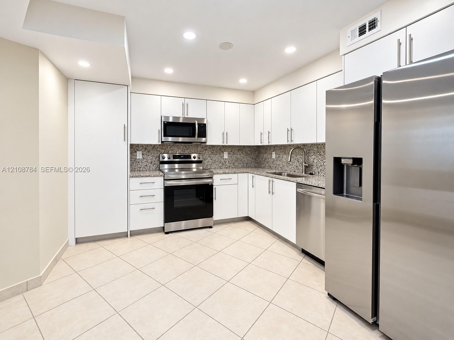 Kitchen featuring white cabinetry, stone-finish countertops, stainless steel appliances, a double-basin undermount sink, and tile flooring