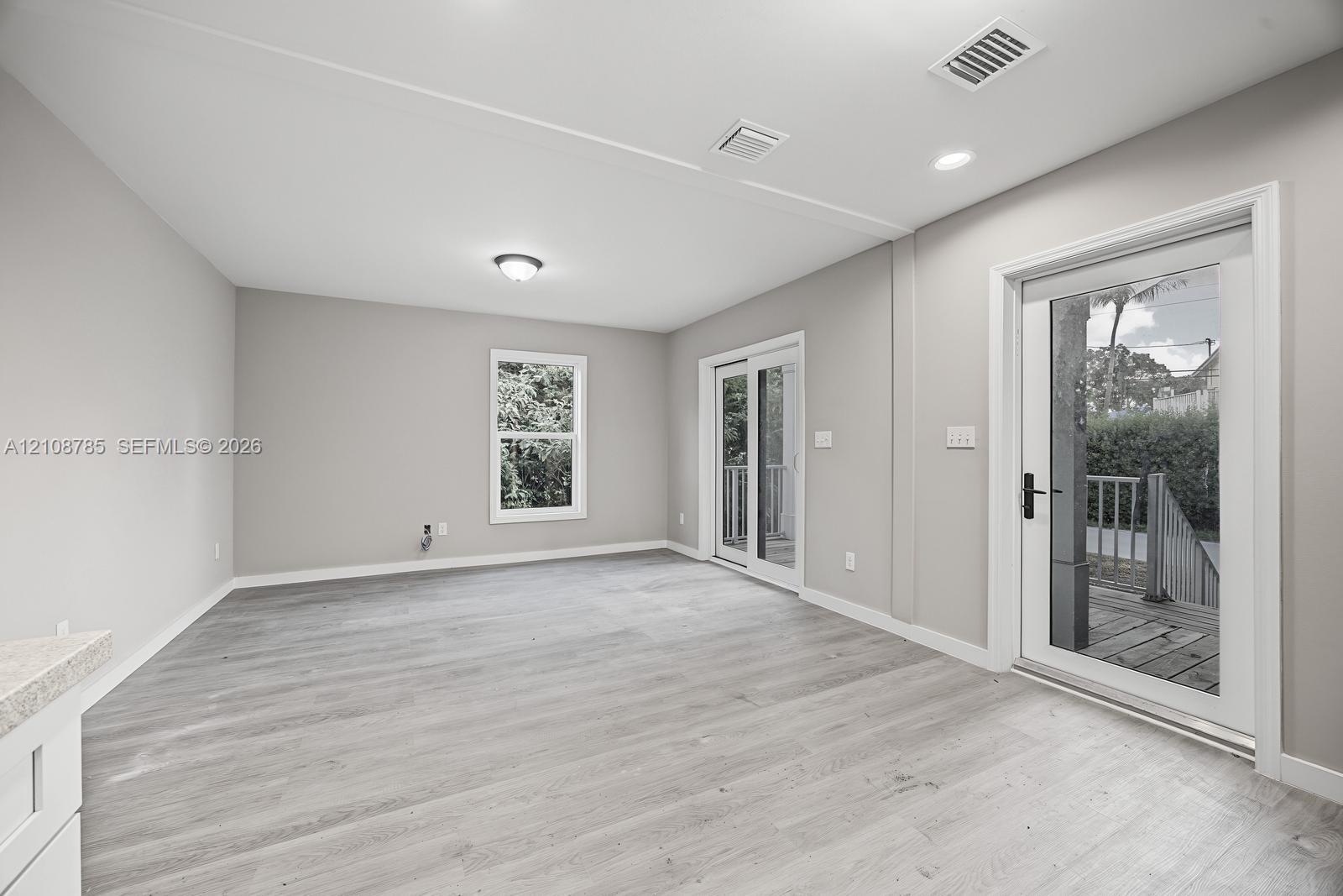 Neutral interior featuring wood-finish flooring, recessed lighting, double glass sliding doors, and a window with exterior greenery