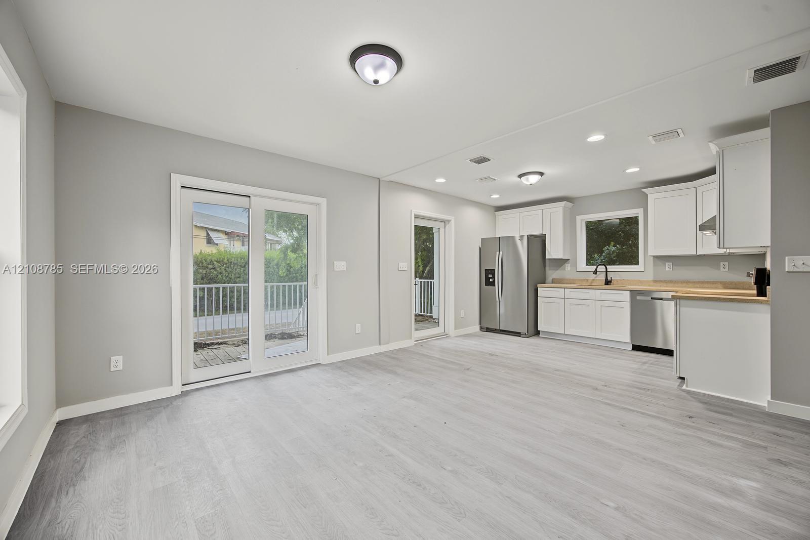 Open-concept space featuring wood-finish flooring, white shaker cabinetry, stainless steel appliances, neutral wall color, and glass sliding door access