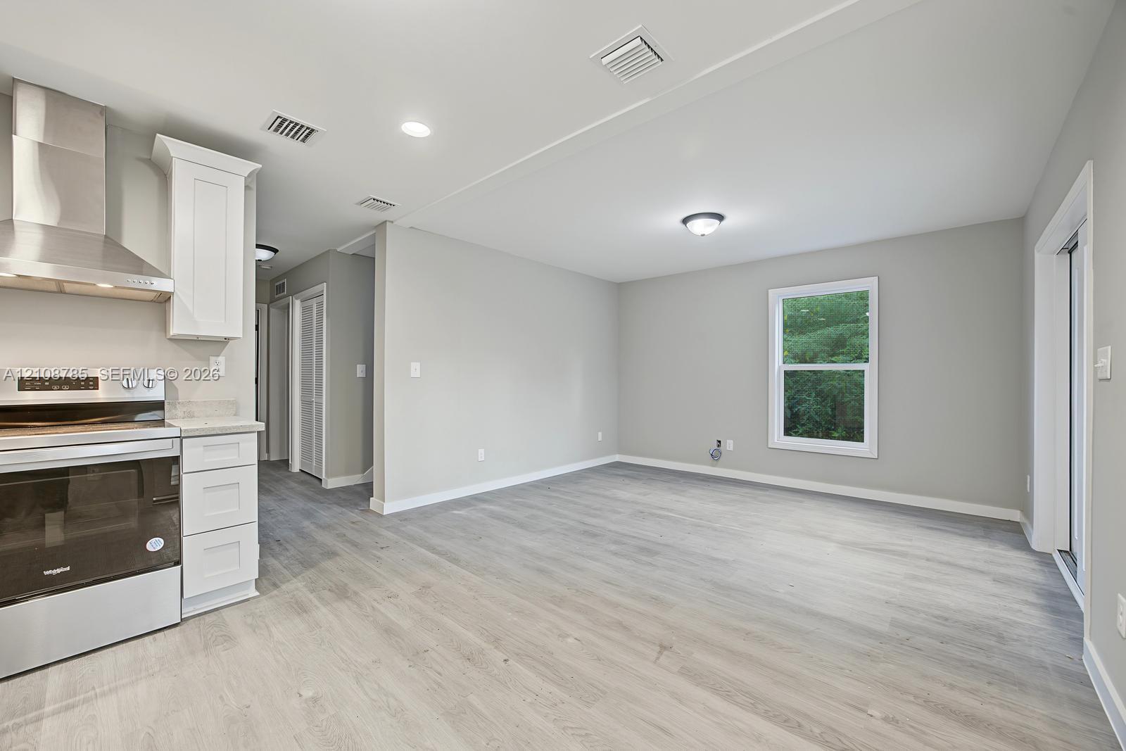 Kitchen featuring stainless steel range, professional-grade range hood, white cabinetry, and wood-finish flooring