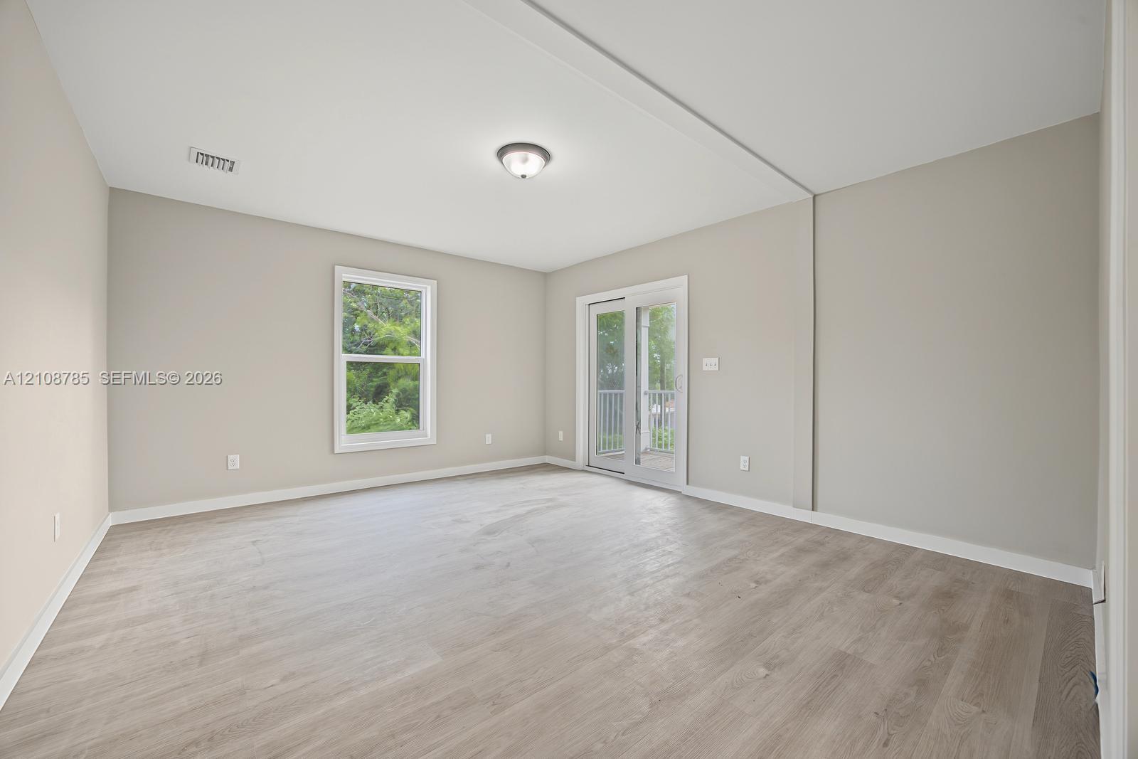Neutral-toned interior featuring wood-finish flooring, a glass-pane sliding door with exterior access, a single window, and a flush-mount ceiling light fixture