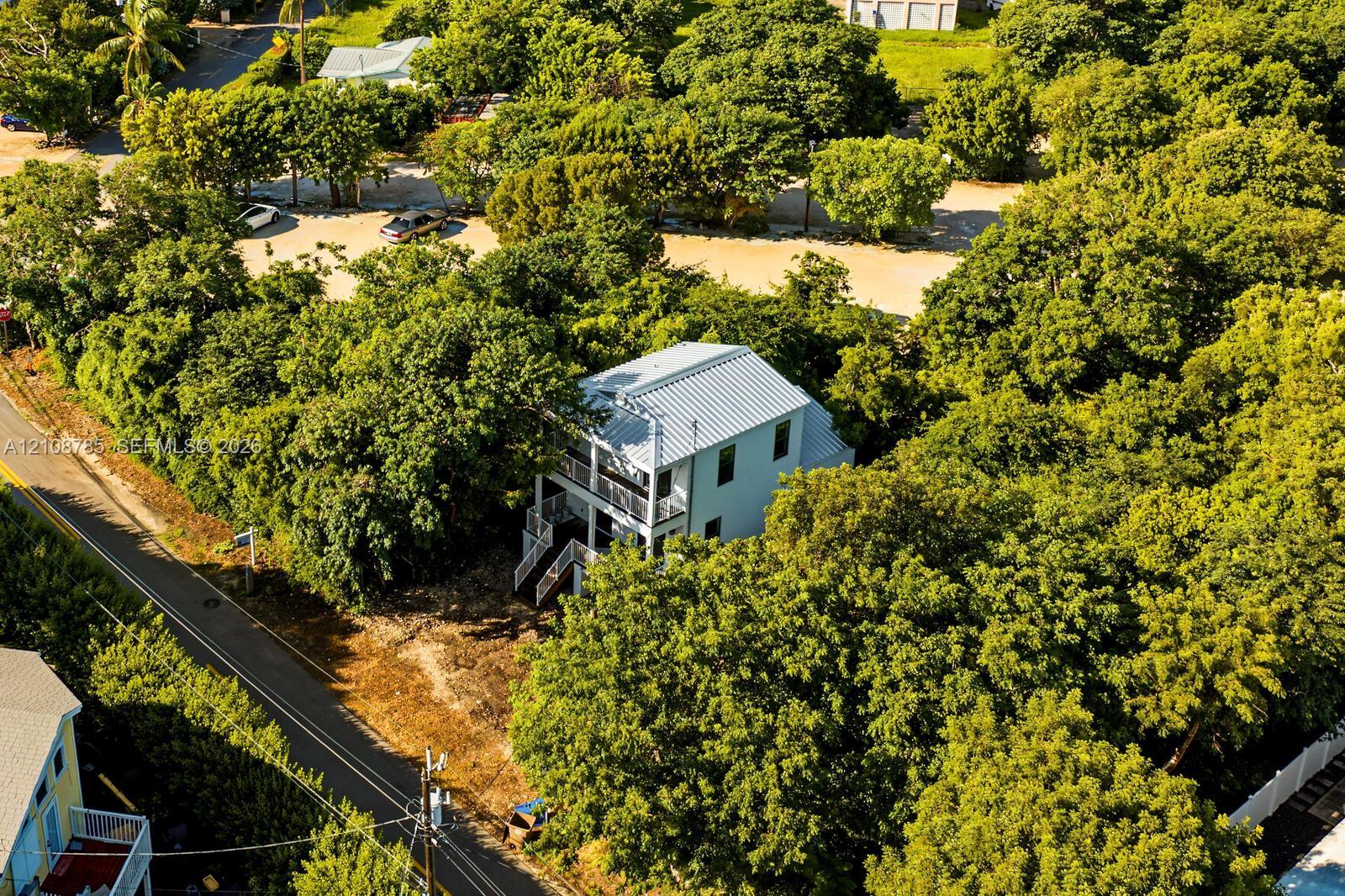Two-story detached residence featuring a metal roof, stacked exterior balconies, and surrounding mature tree canopy