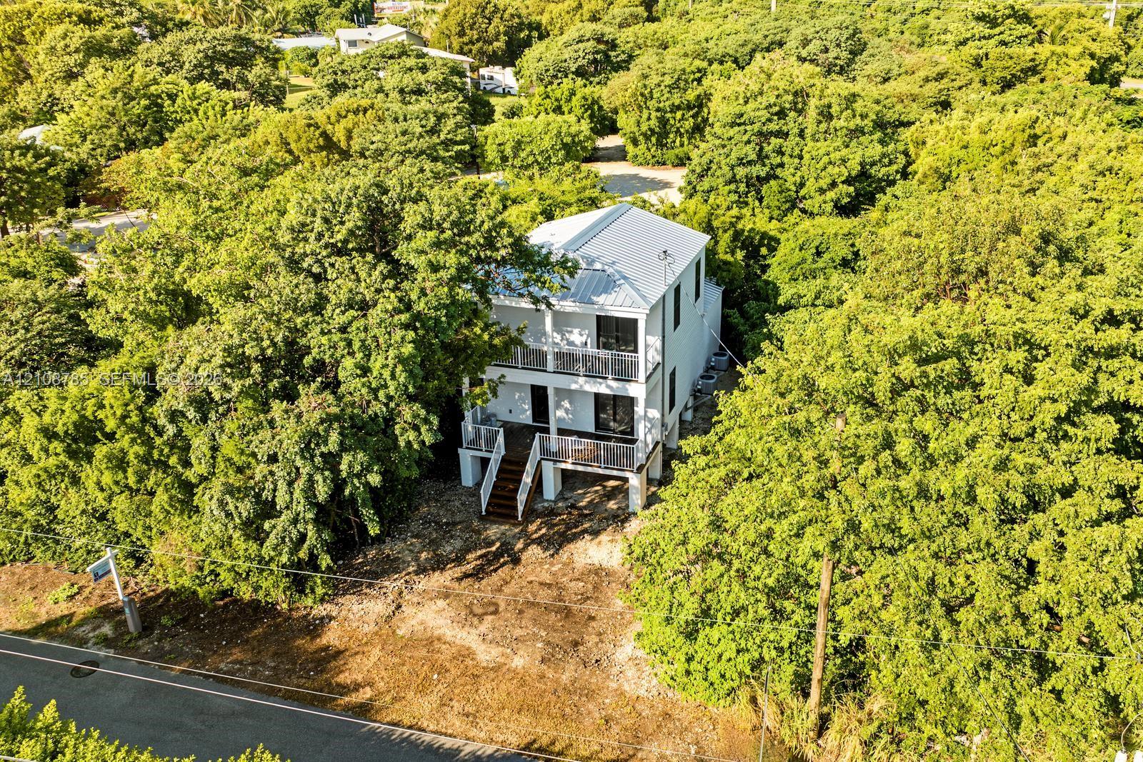 Two-story residence featuring a metal roof, stacked porches with metal railings, and elevated construction, situated on a lot with mature trees