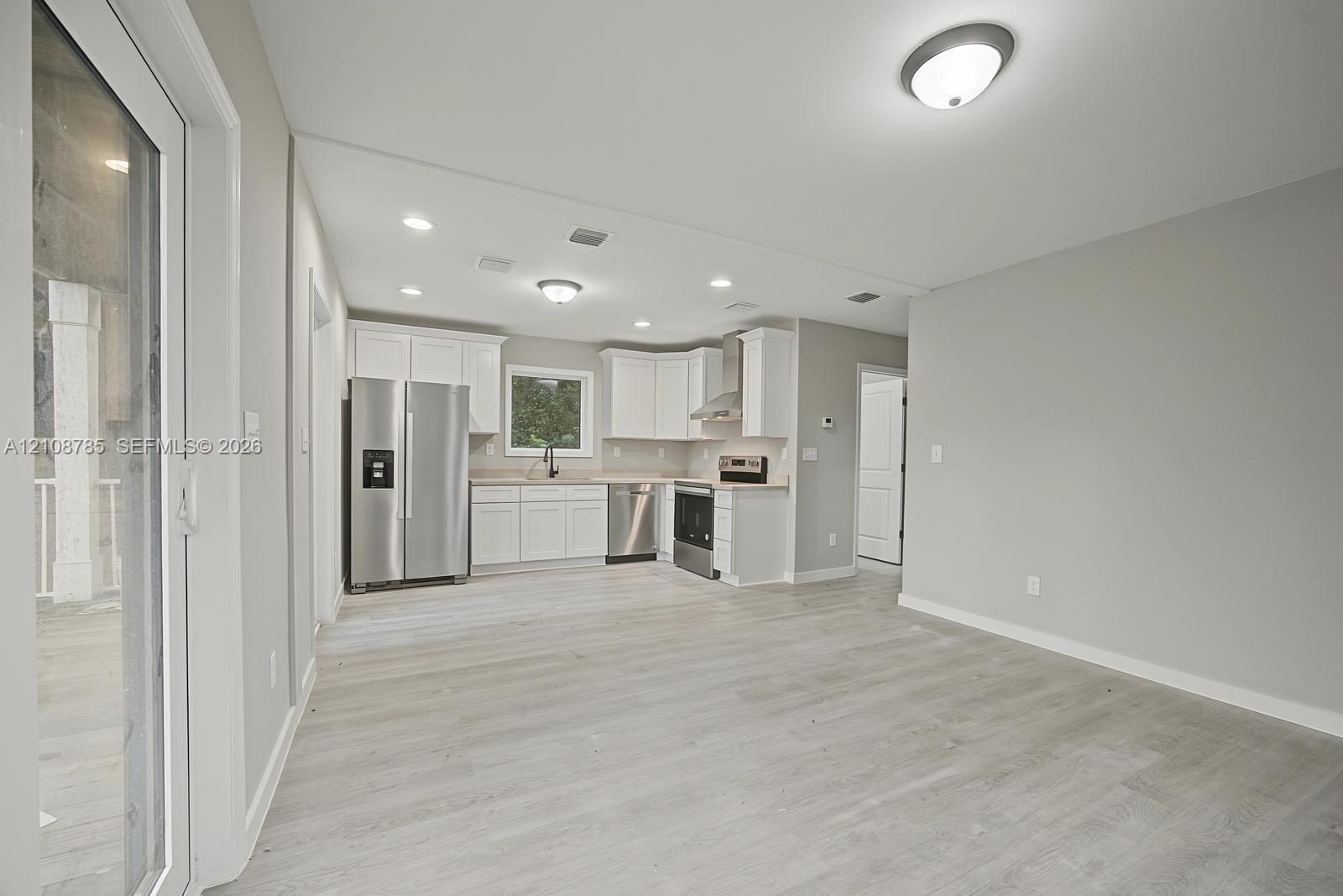 Kitchen featuring white cabinetry, stainless steel appliances, wood-finish flooring, recessed lighting, and a sliding glass door
