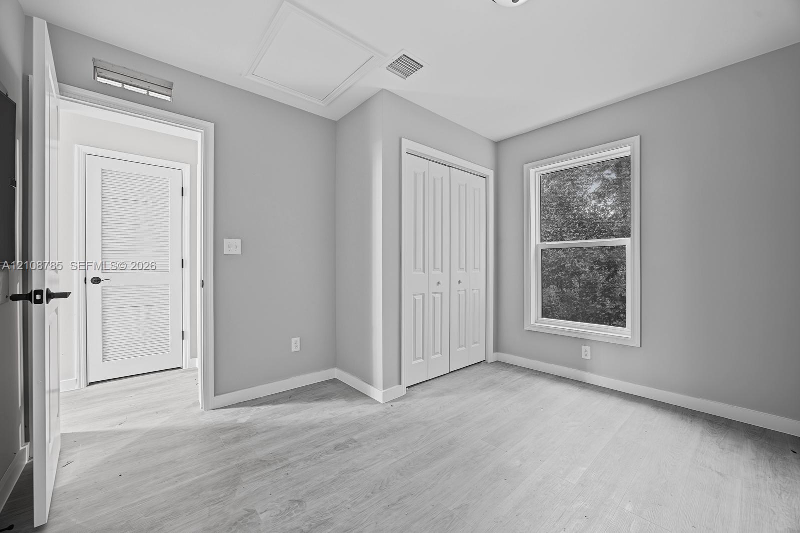 Interior space featuring neutral wall paint, wood-finish flooring, double-panel closet doors, and a single-hung window with exterior greenery