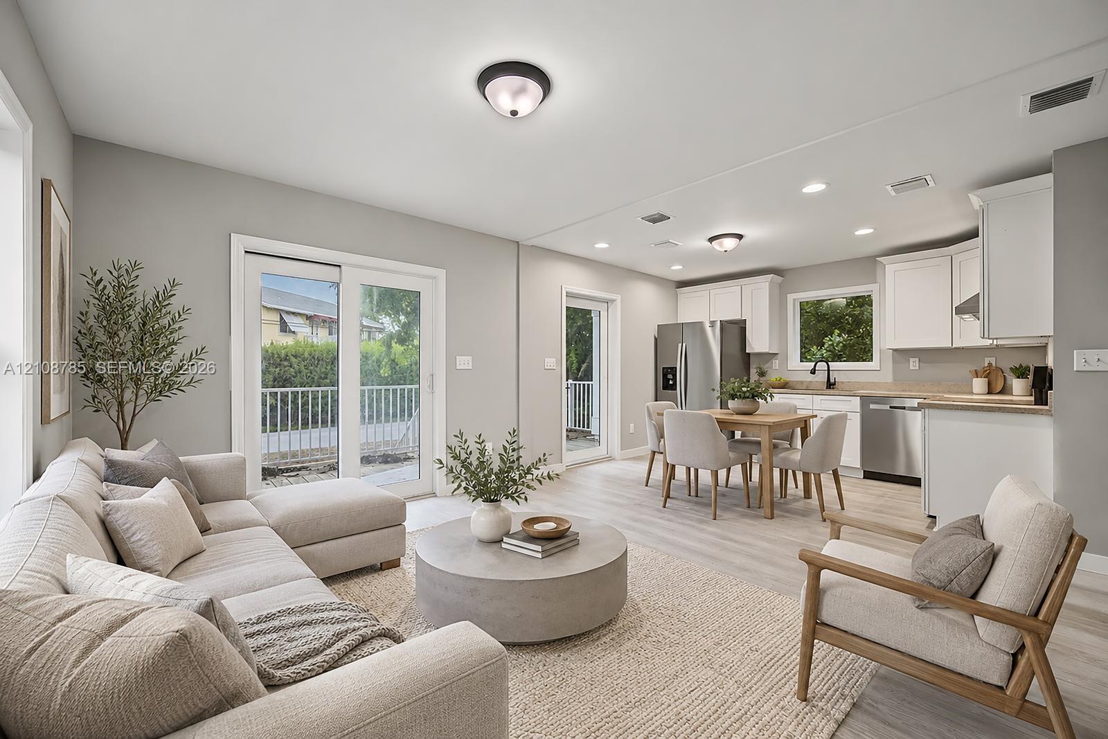 Open-concept living space featuring wood-finish flooring, white cabinetry, stainless steel appliances, recessed lighting, and glass sliding doors
