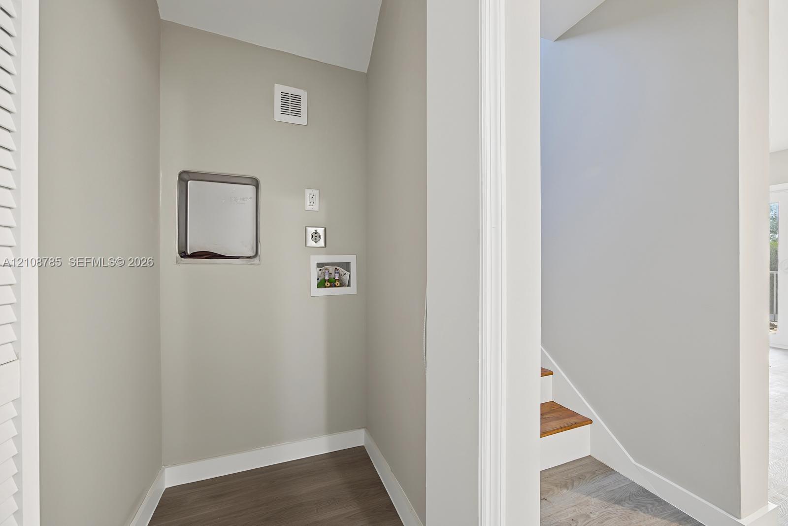 Neutral interior alcove featuring wood-finish flooring and integrated wall-mounted utility access panels