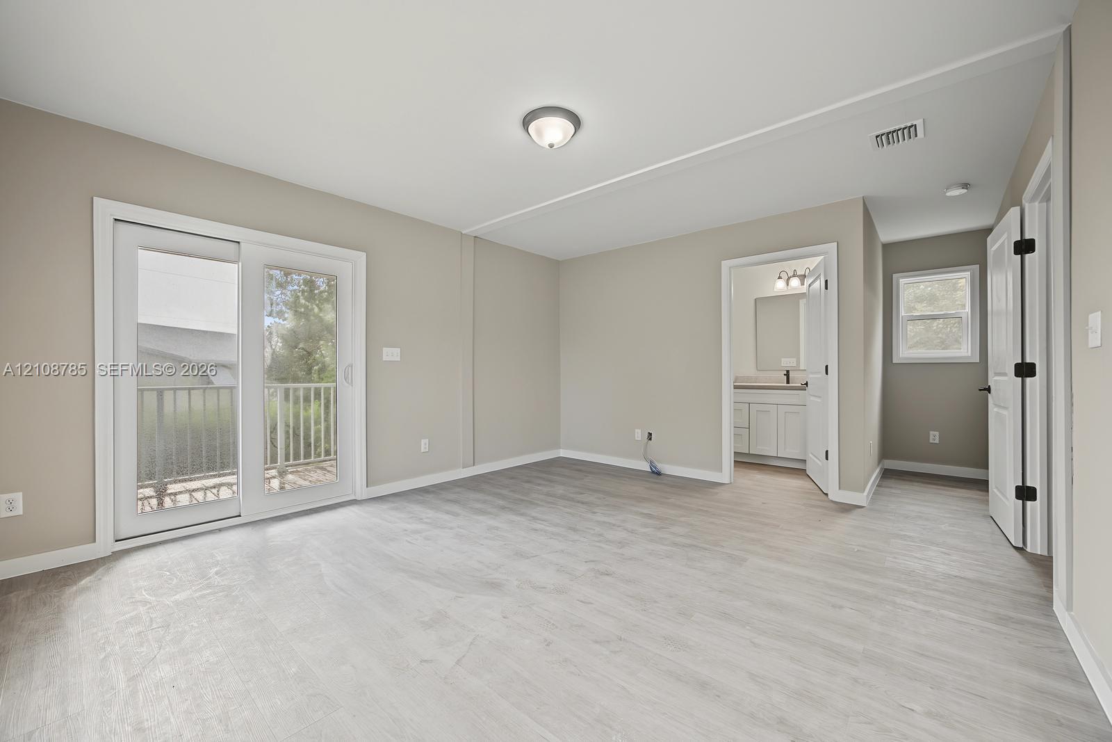 Neutral wall-toned room featuring wood-finish flooring, white sliding glass door, flush-mount ceiling lighting, and crisp white trim