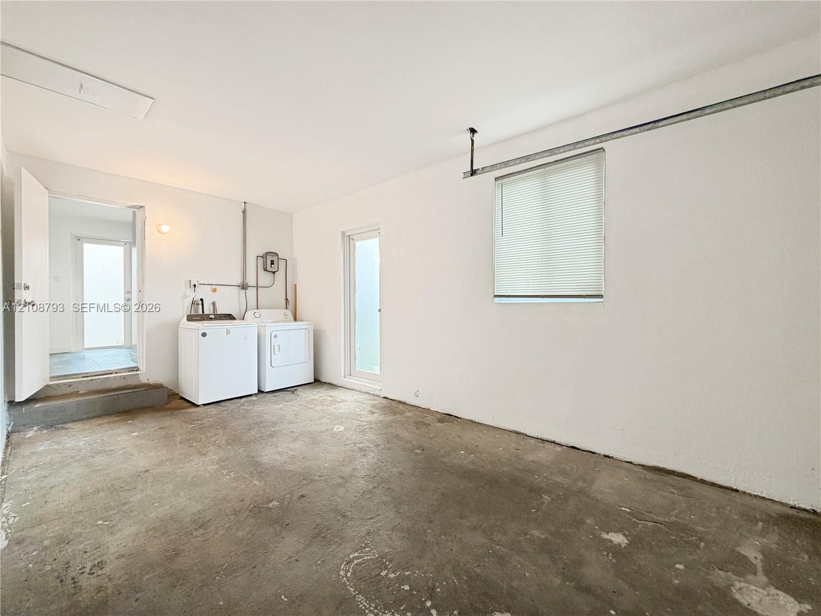 Utility area featuring concrete flooring, white walls, and a window with integrated blinds