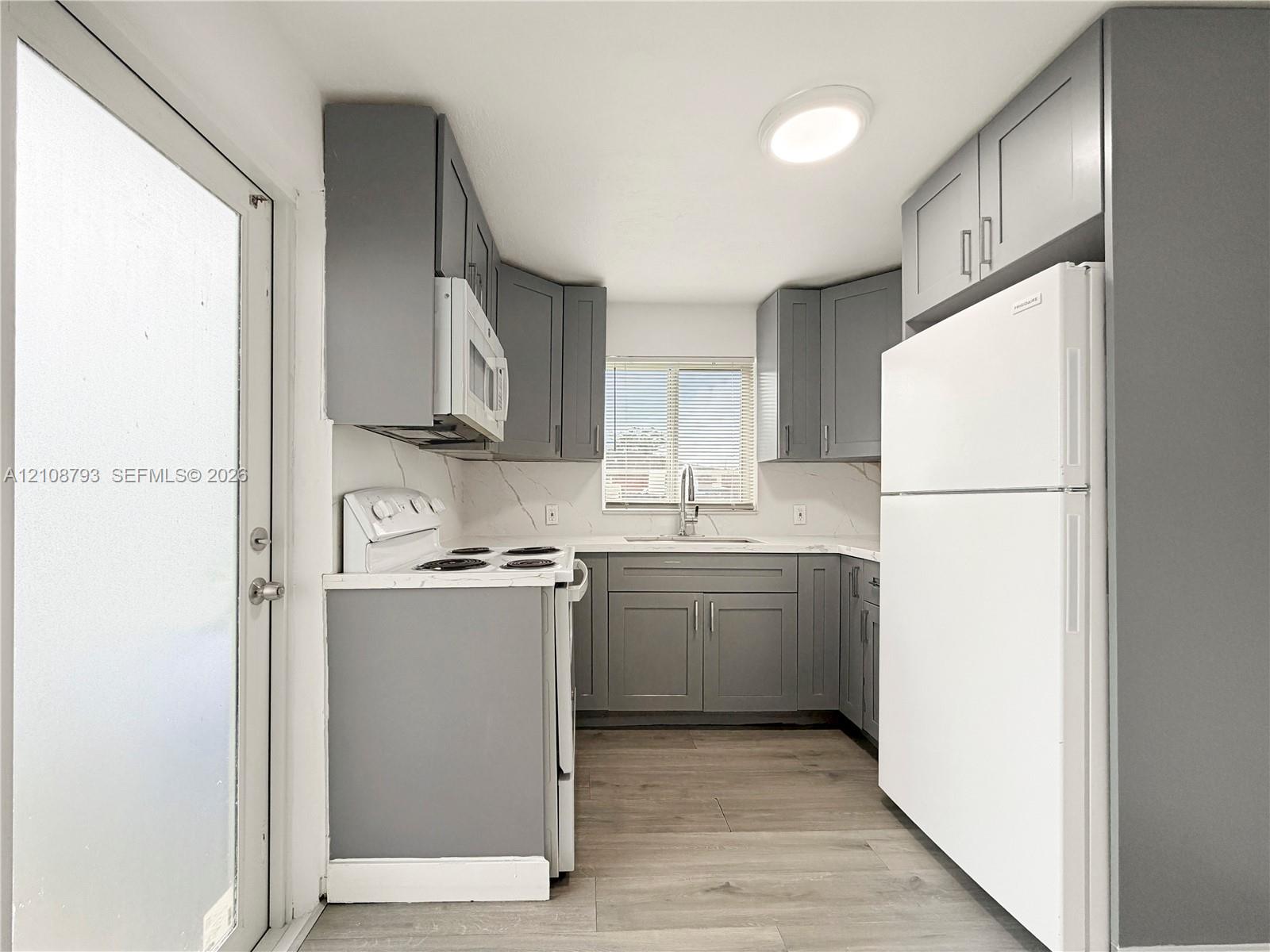 Kitchen featuring grey shaker-style cabinetry, solid-surface countertops with backsplash, wood-finish flooring, and white appliances