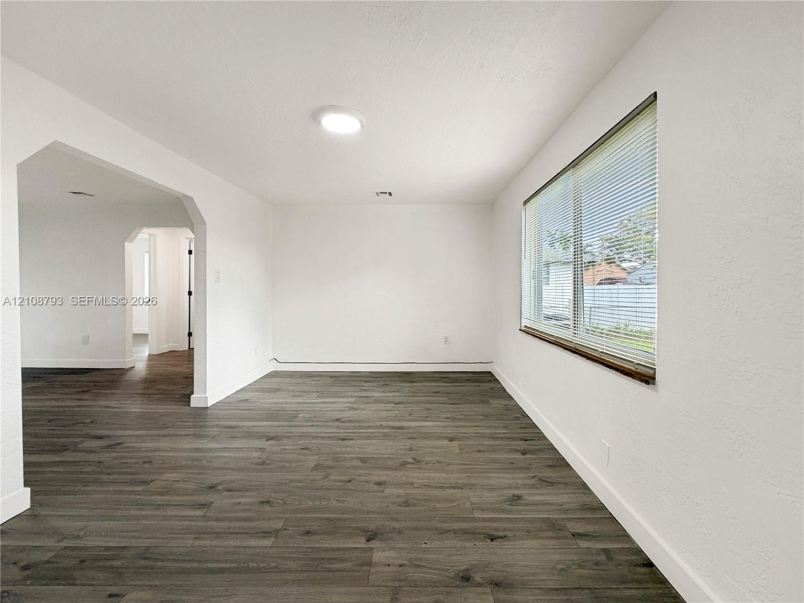 Interior space featuring wood-finish flooring, a large window with horizontal blinds, and a wide arched opening