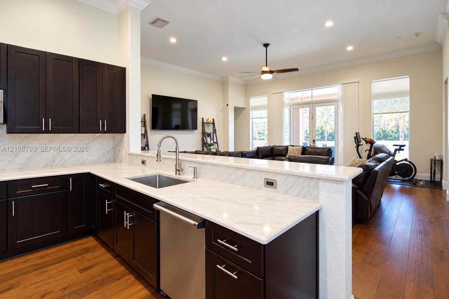 Kitchen featuring dark-finish cabinetry, stone-surface countertops, stone-surface backsplash, stainless steel undermount sink, and wood-finish flooring