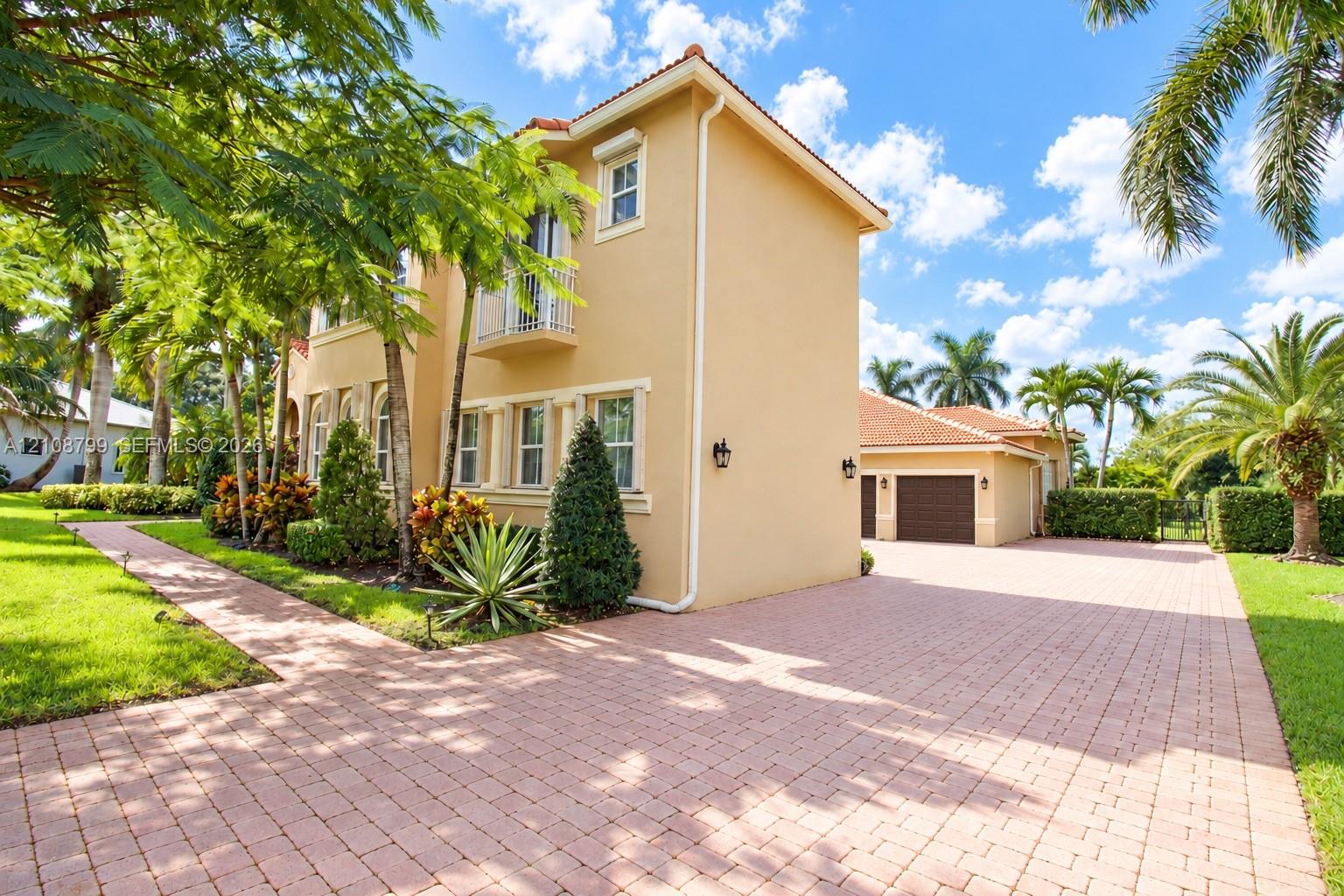 Two-story stucco exterior featuring a tile roof, an upper-level balcony, a paved brick driveway, and an attached multi-car garage