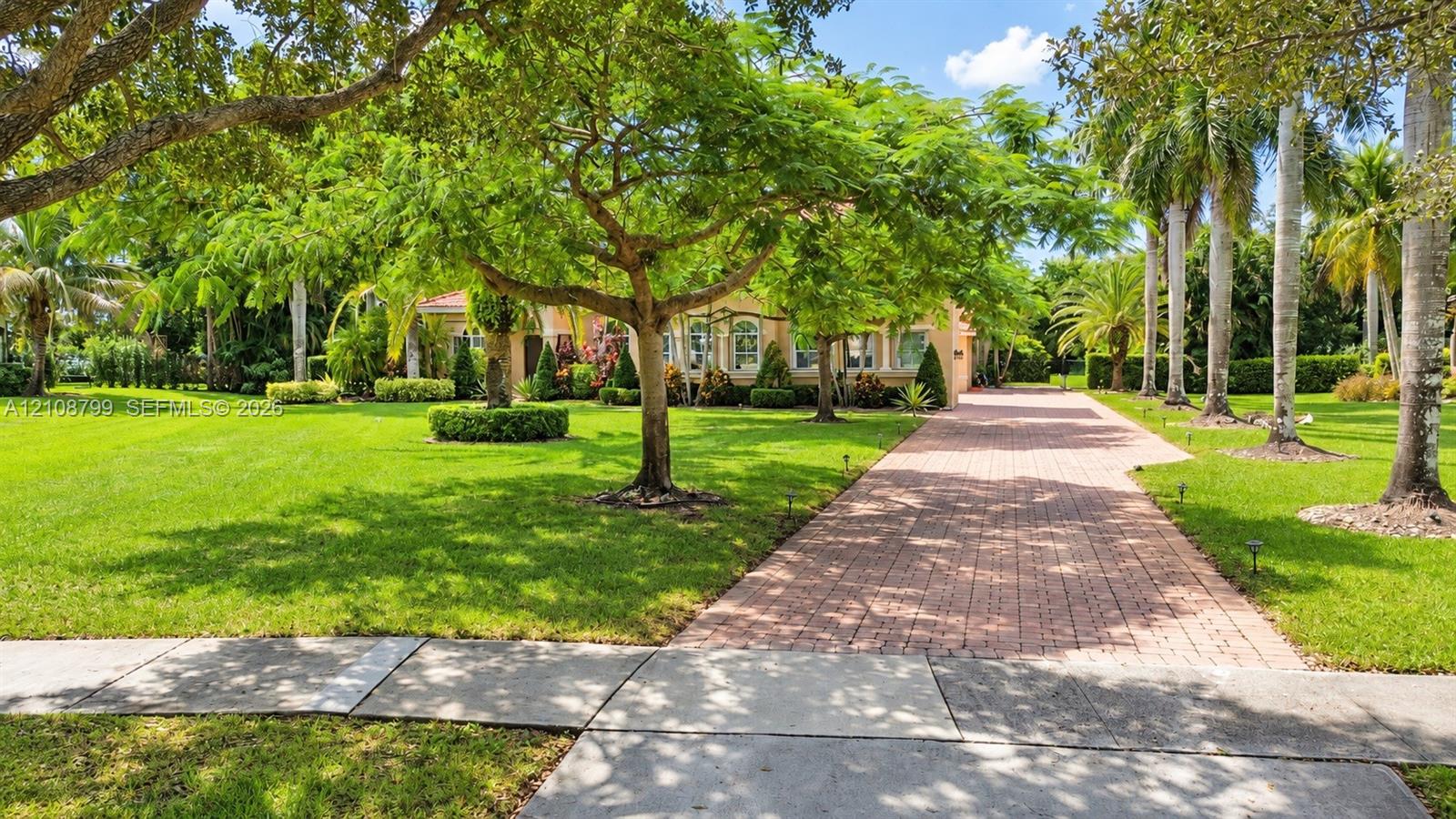 Expansive lawn featuring mature tropical landscaping, palm trees, and a paved brick driveway