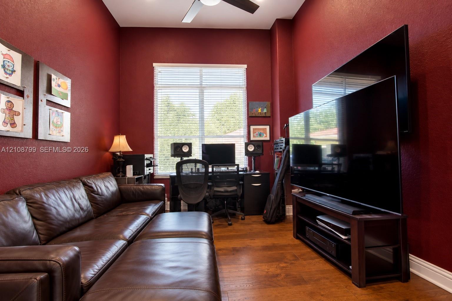 Room featuring high ceilings, wood-finish flooring, a large window with horizontal blinds, and a ceiling fan with integrated lighting
