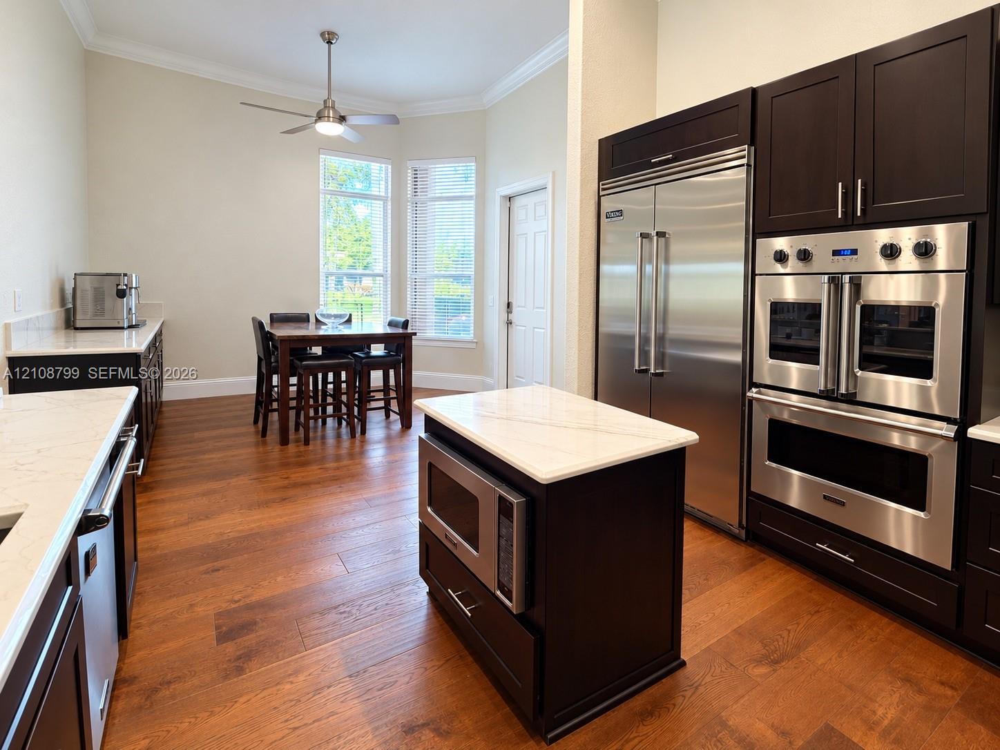 Kitchen featuring dark cabinetry, stone-finish countertops, stainless steel professional-grade double wall ovens, a side-by-side refrigerator, and wood-finish flooring