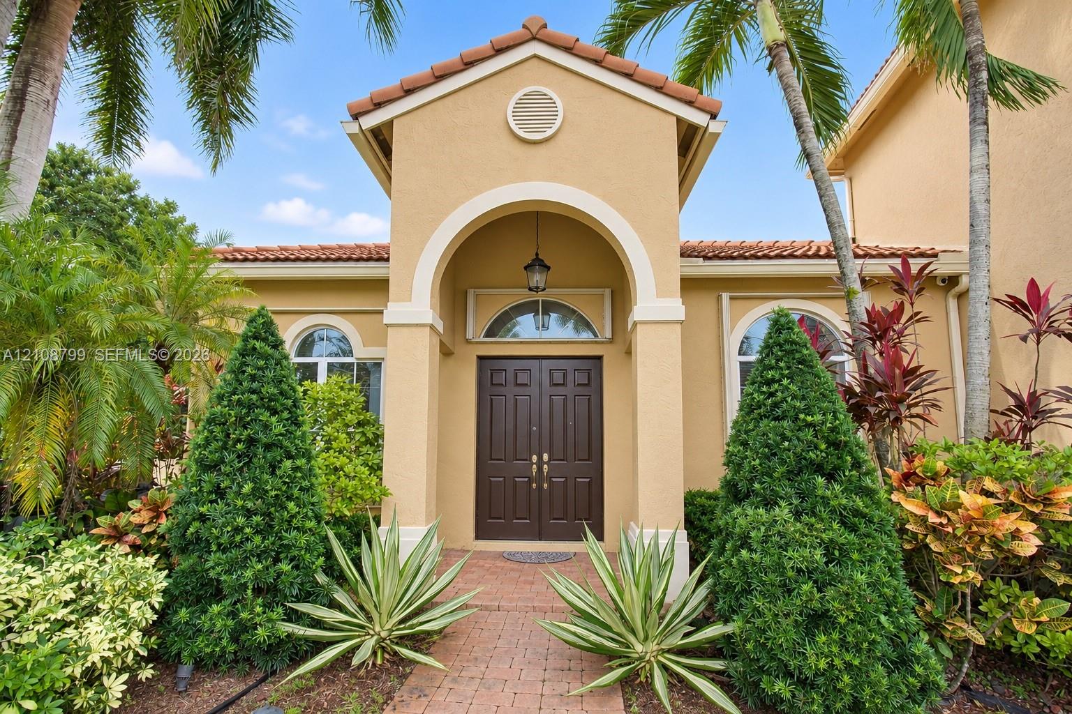 Stucco exterior featuring a covered portico entrance, arched entryway, double-door main entry, and clay tile roof
