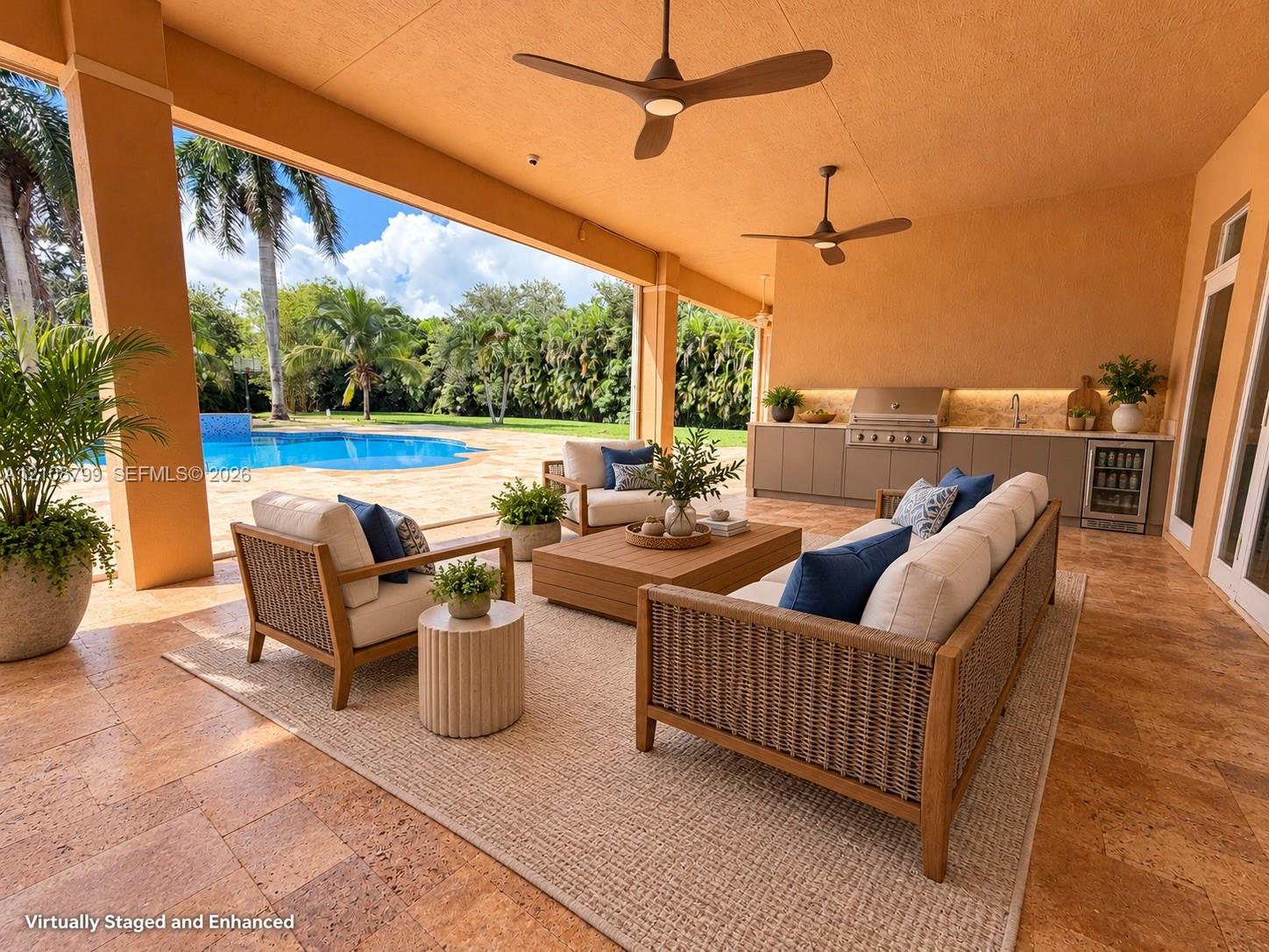 Covered outdoor living space featuring stone flooring, dual ceiling fans, built-in outdoor kitchen with stainless steel grill, and an in-ground swimming pool