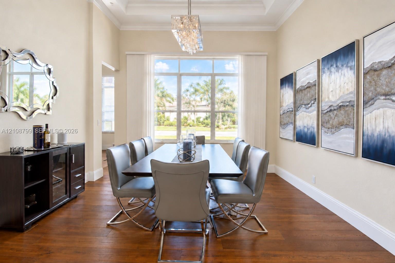 Formal dining area featuring tray ceilings, wood-finish flooring, and a large multi-pane window