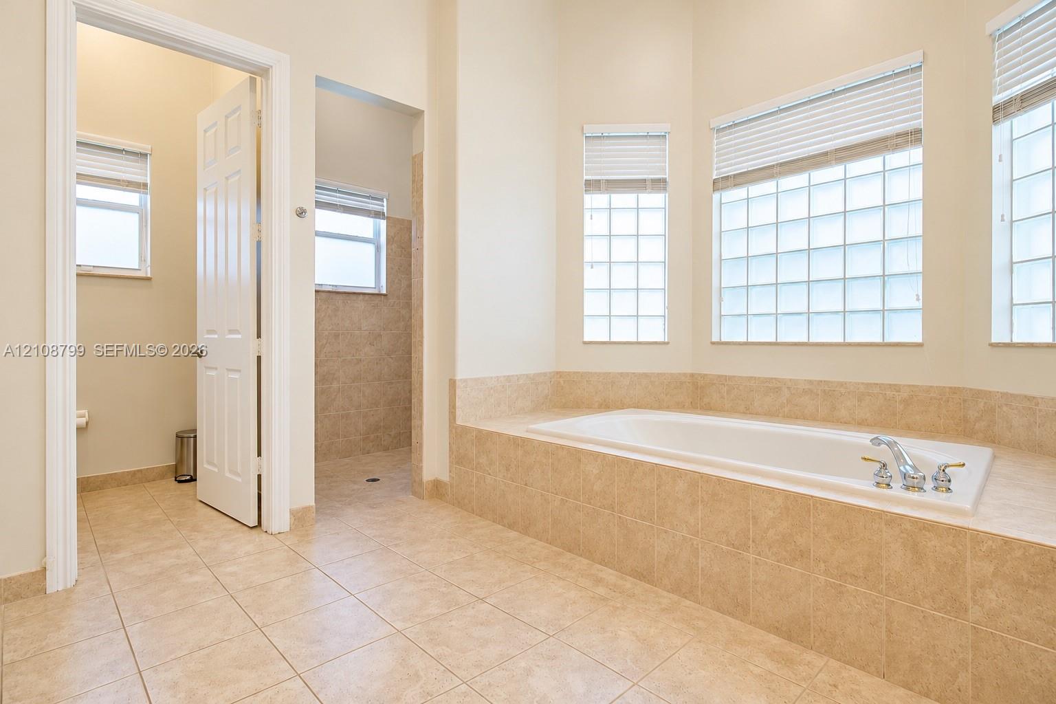 Soaking tub set in a tile-surround deck, tile flooring, glass block windows, and a separate walk-in shower enclosure