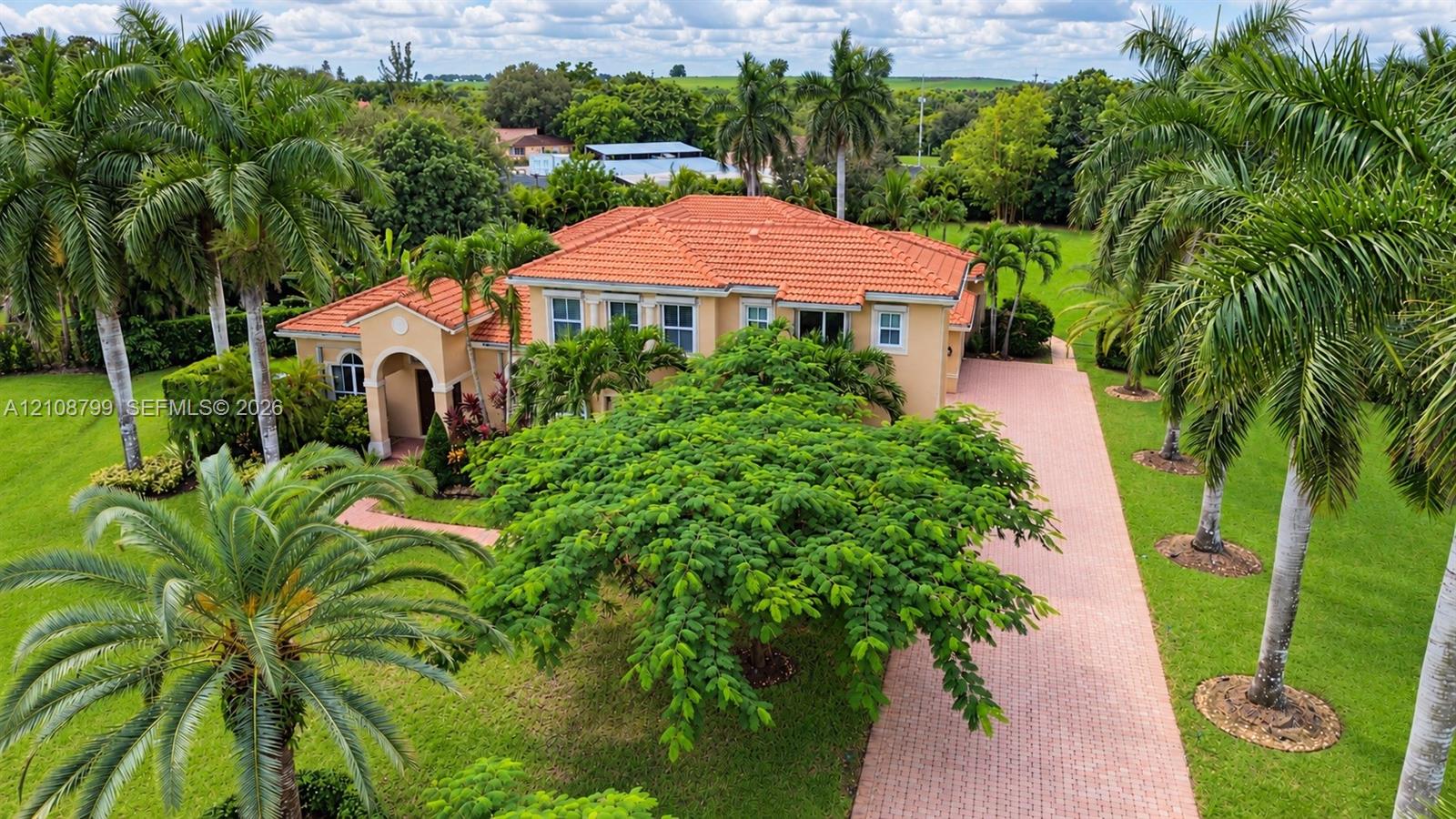 Stucco exterior featuring a terracotta-tiled roof, an arched entryway, a paved driveway, and mature landscaping