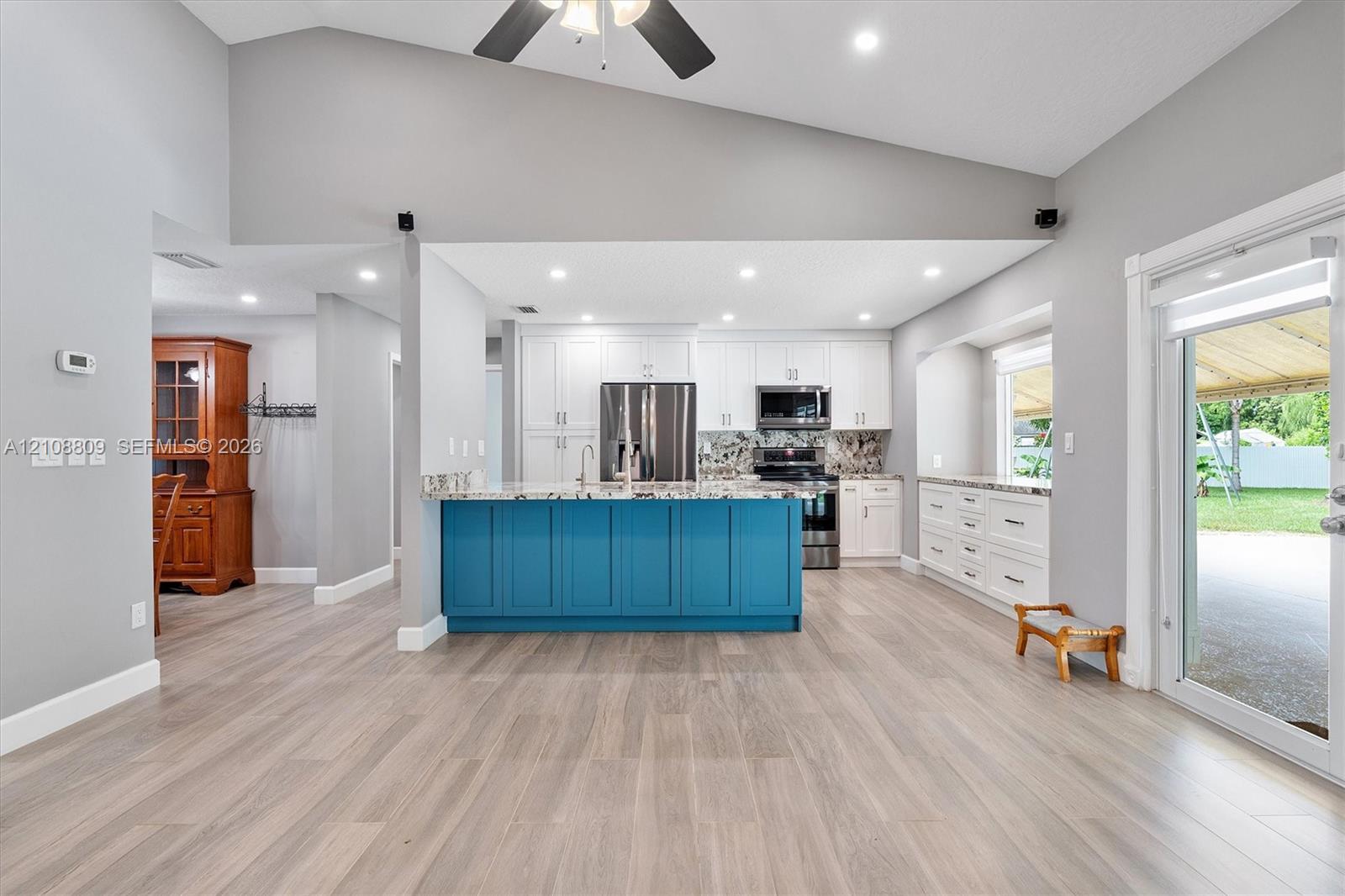 Kitchen featuring wood-finish flooring, vaulted ceilings, a central island with a saturated blue finish, white cabinetry, and stainless-steel appliances