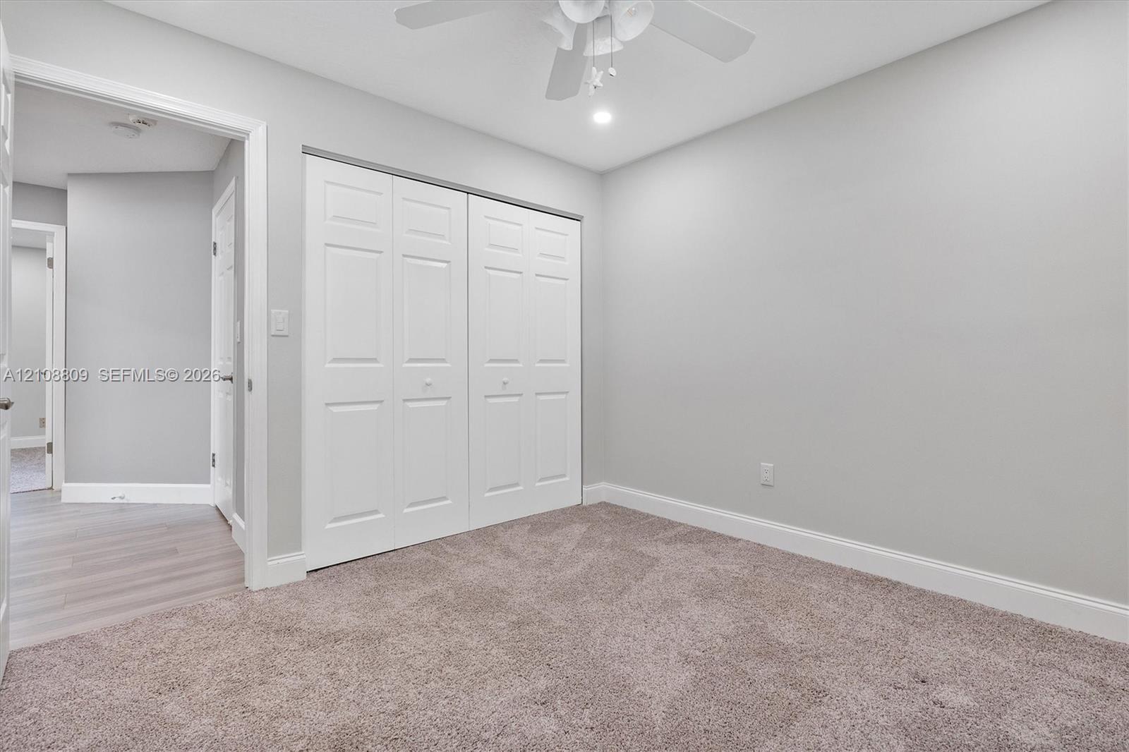 Neutral-toned wall paint, plush carpeting, ceiling fan with integrated lighting, and double-panel closet doors