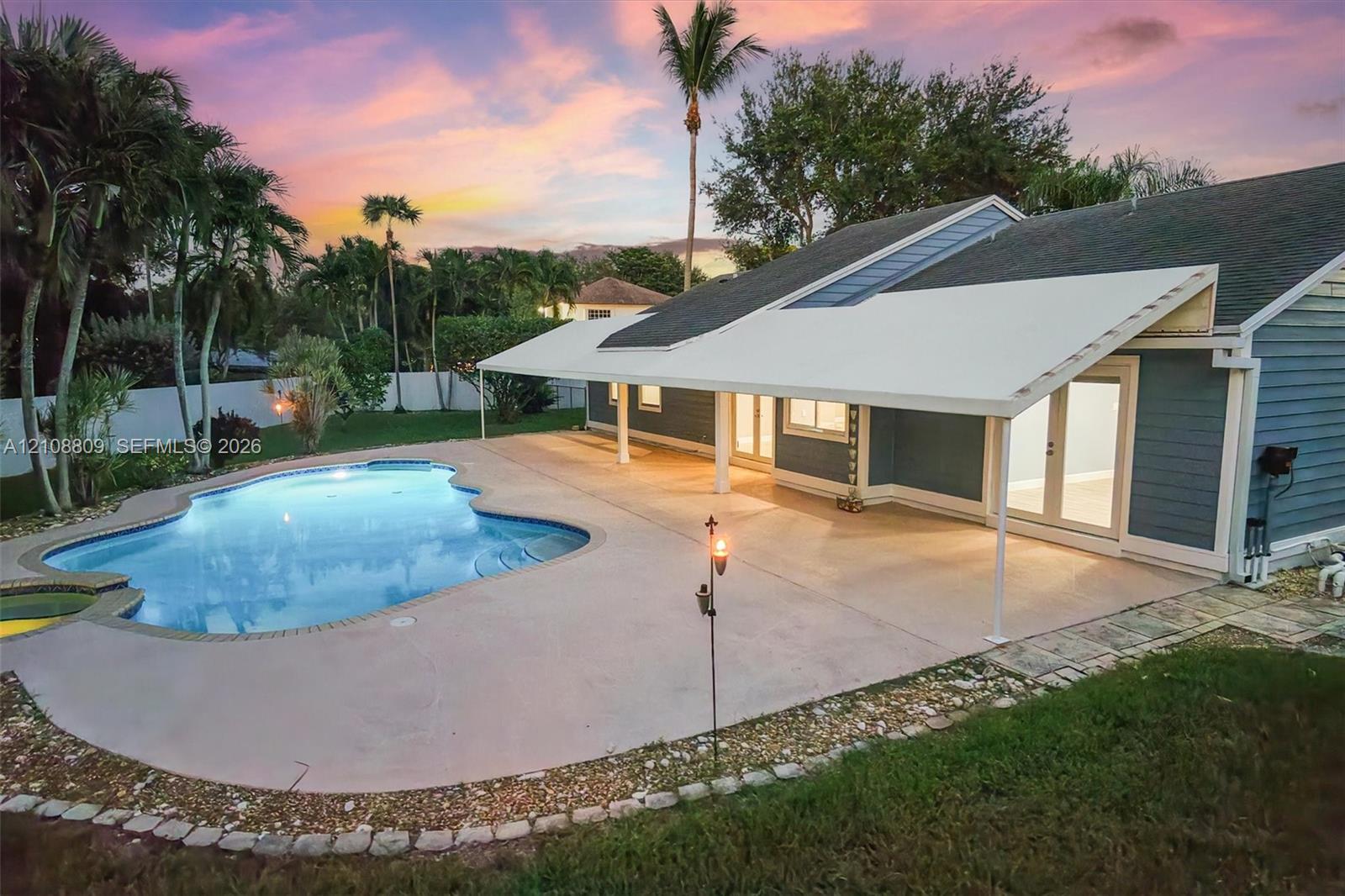 Rear exterior featuring a freeform swimming pool, extensive concrete patio, covered lanai, lap siding, and multi-pane glass doors