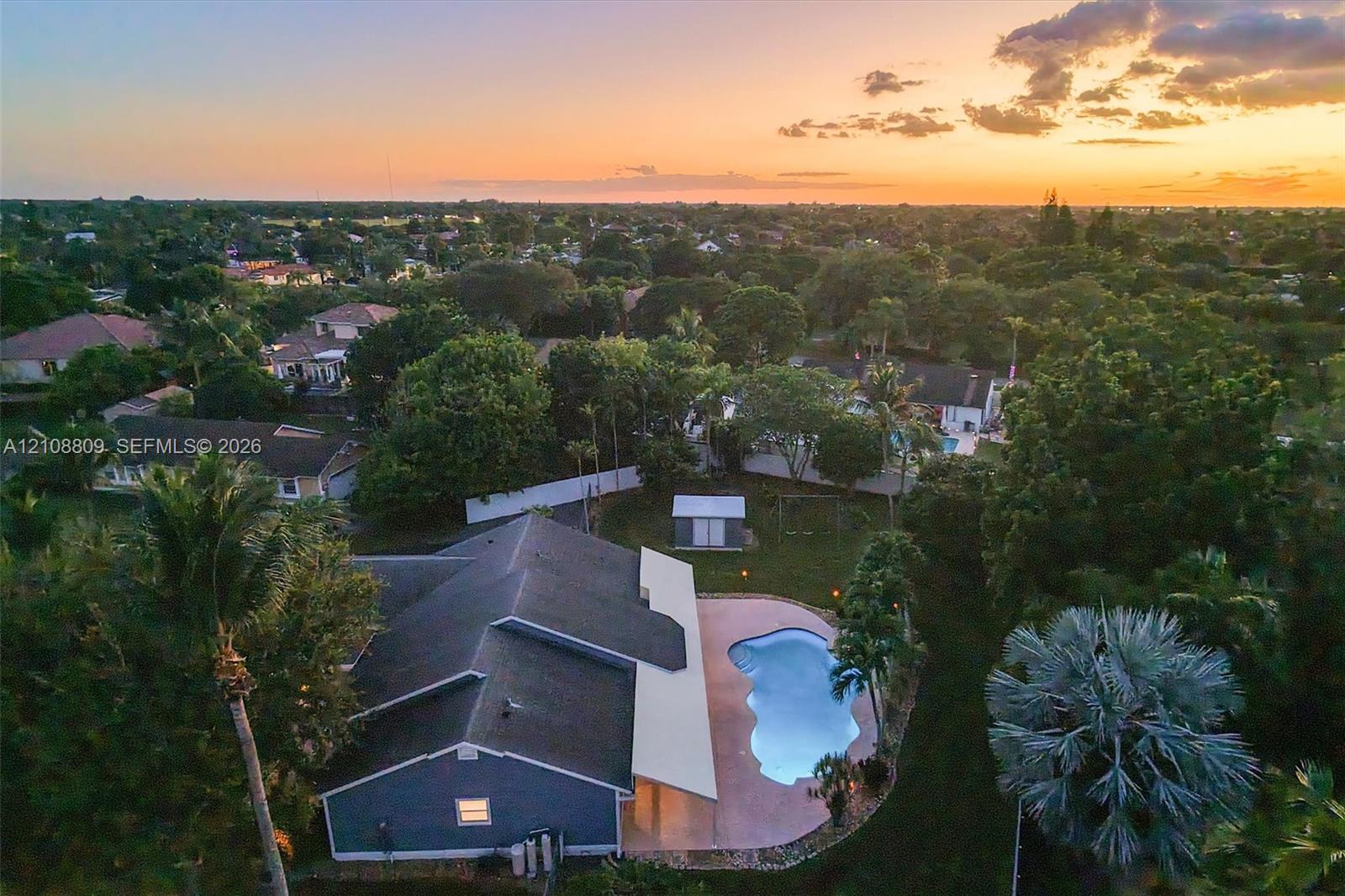 Aerial perspective of a property featuring an in-ground swimming pool, concrete patio, detached storage structure, and mature landscaping