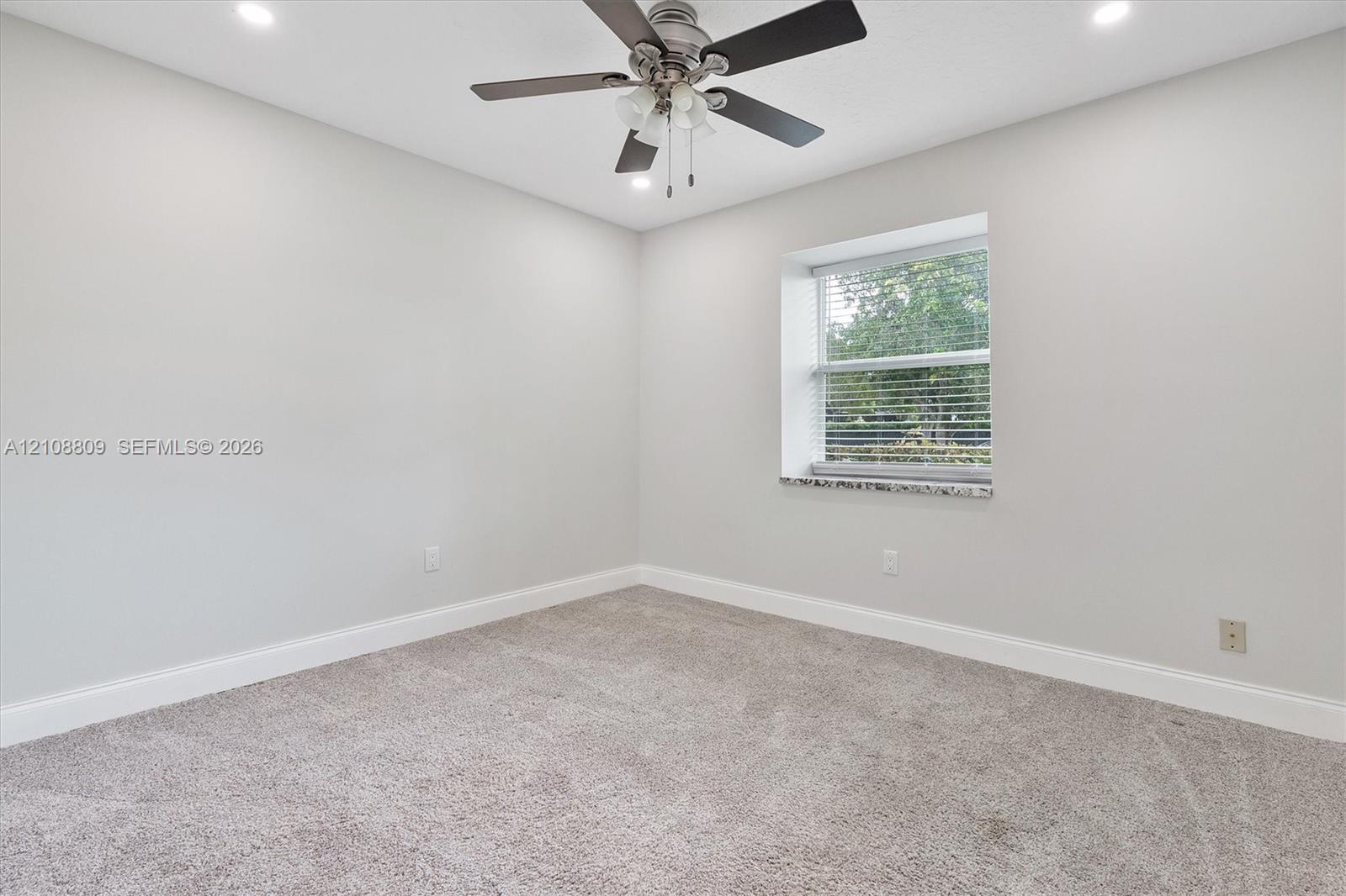 Neutral interior room featuring recessed lighting, a multi-blade ceiling fan with integrated light fixture, neutral carpeting, and a window sill finished in polished stone