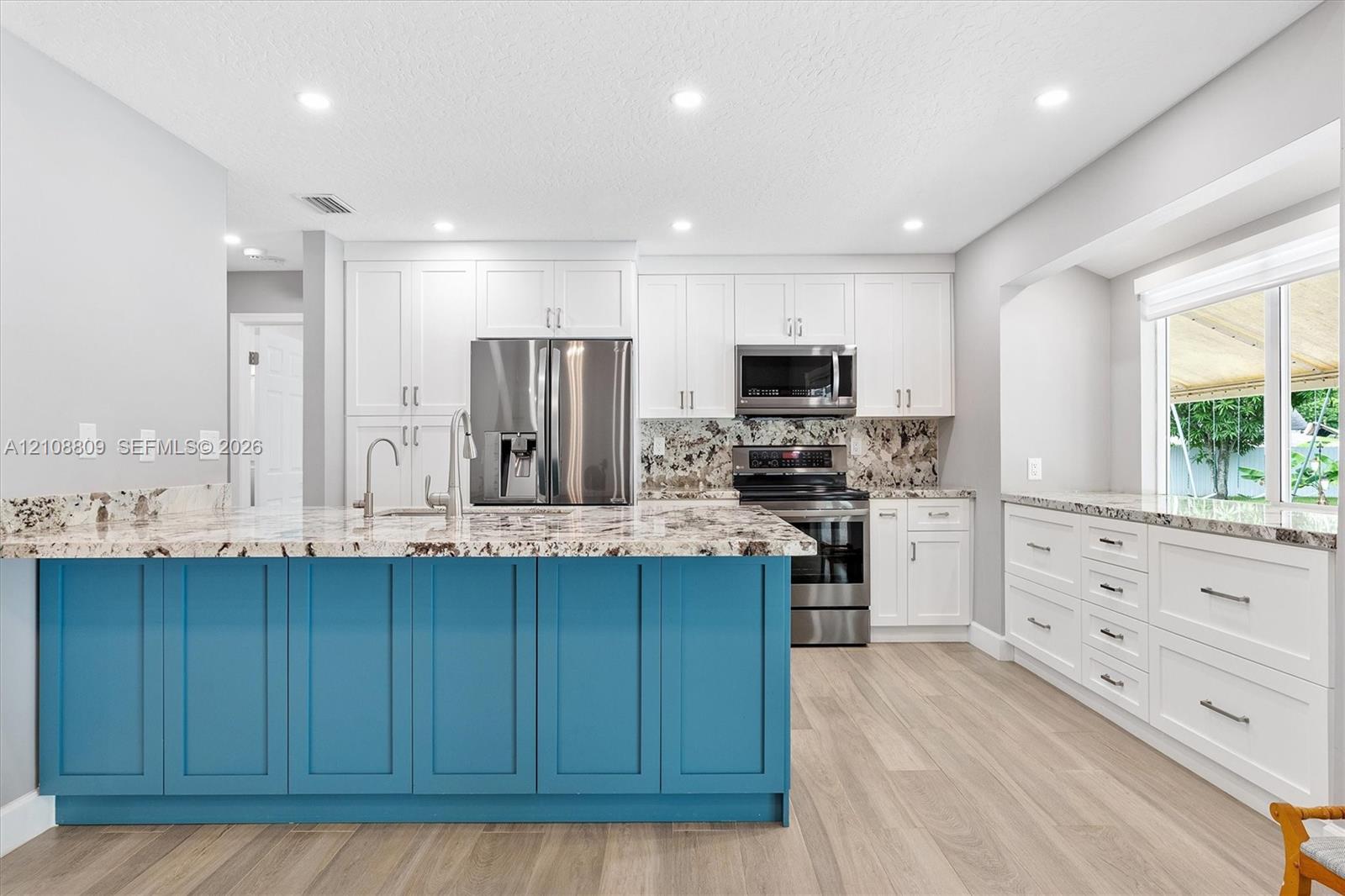Kitchen featuring a blue-accented center island, white cabinetry, stone-finish countertops, stainless steel appliances, and wood-finish flooring