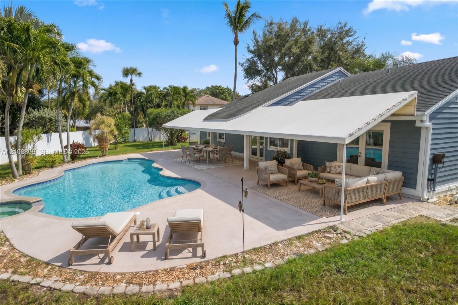 In-ground swimming pool with integrated spa, concrete patio, retractable awning, and lap siding exterior
