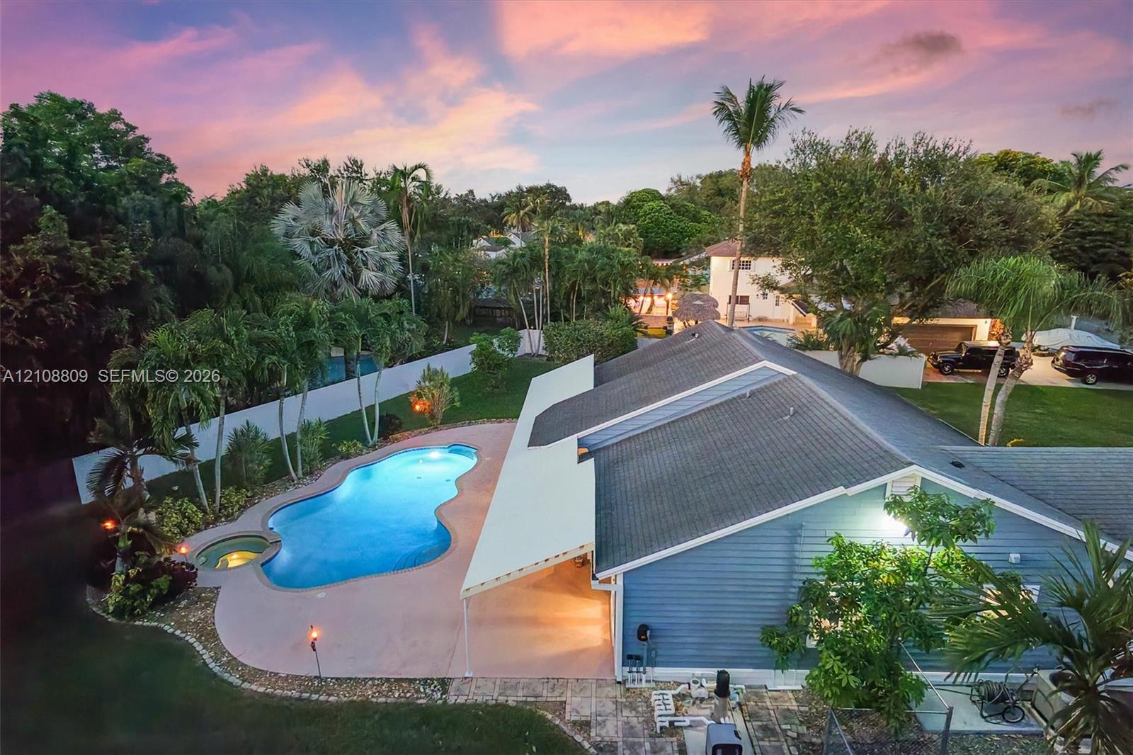 Backyard featuring an in-ground swimming pool with an integrated spa, a concrete pool deck, a covered patio, and mature landscaping