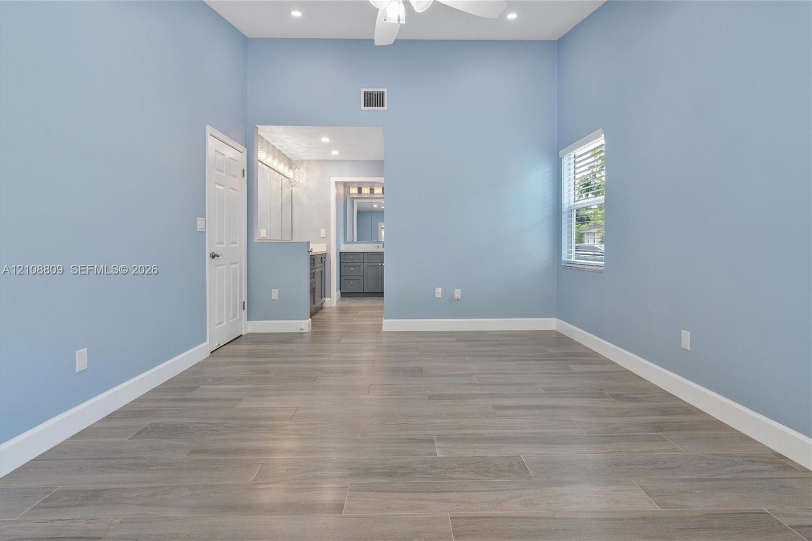 Room featuring high ceilings, wood-finish tile flooring, recessed lighting, and a dual-pane window with white blinds