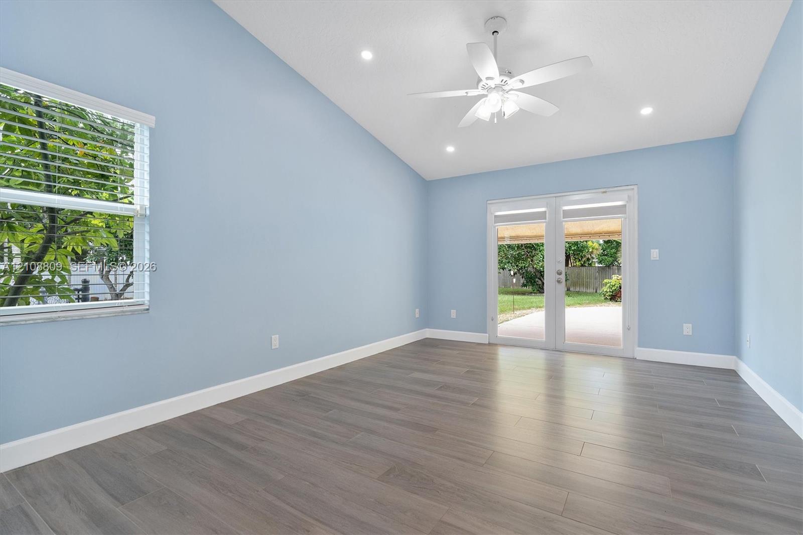 Vaulted ceiling with recessed lighting, wood-finish flooring, white ceiling fan with integrated lighting, horizontal window blinds, and dual-pane glass entry doors