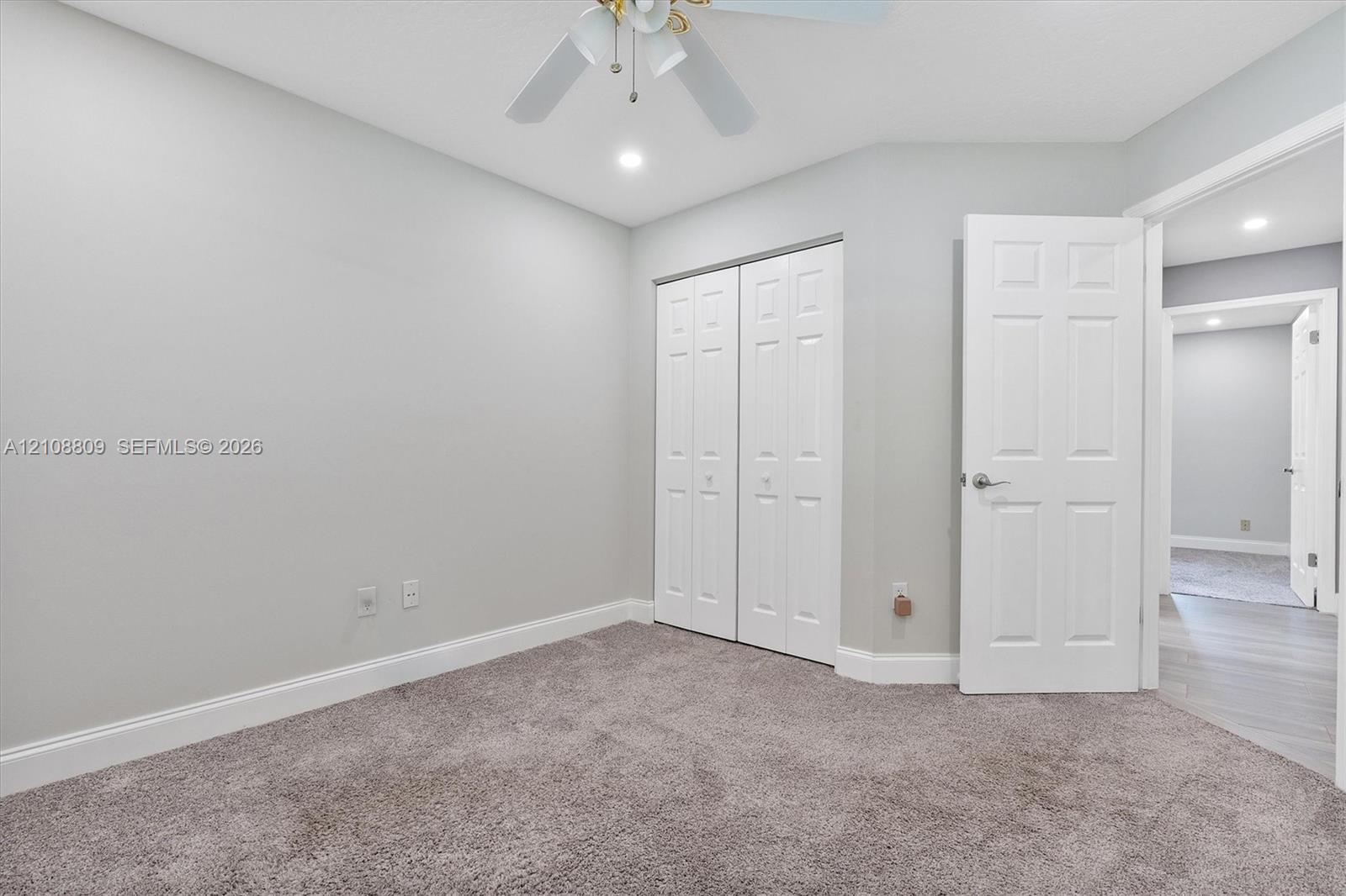Neutral wall tones, carpeted flooring, bi-fold closet doors, six-panel interior door, and a ceiling-mounted light fixture with a fan