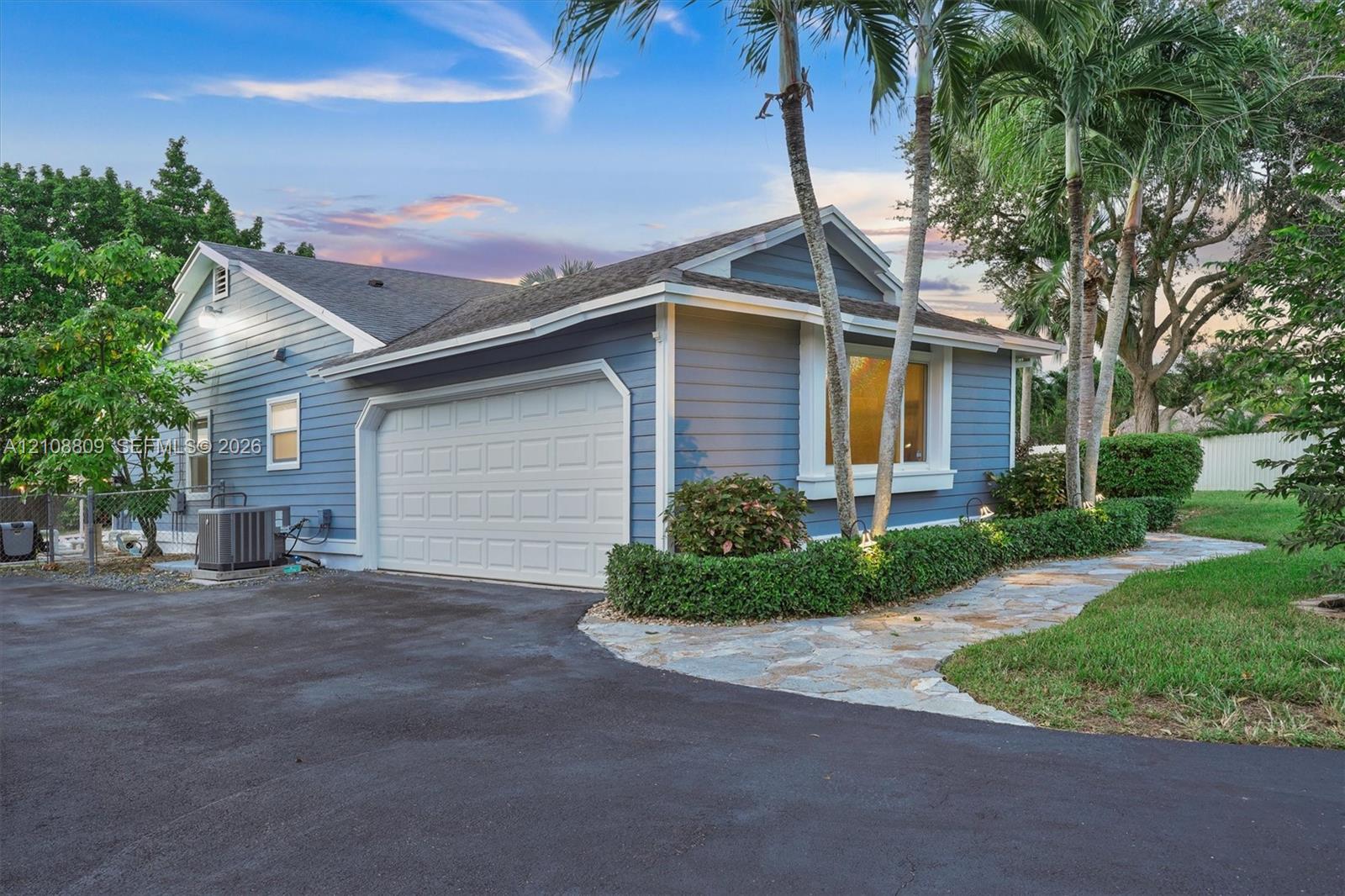 Single-story exterior featuring blue lap siding, a paved driveway, a multi-car garage, and stone-style walkway