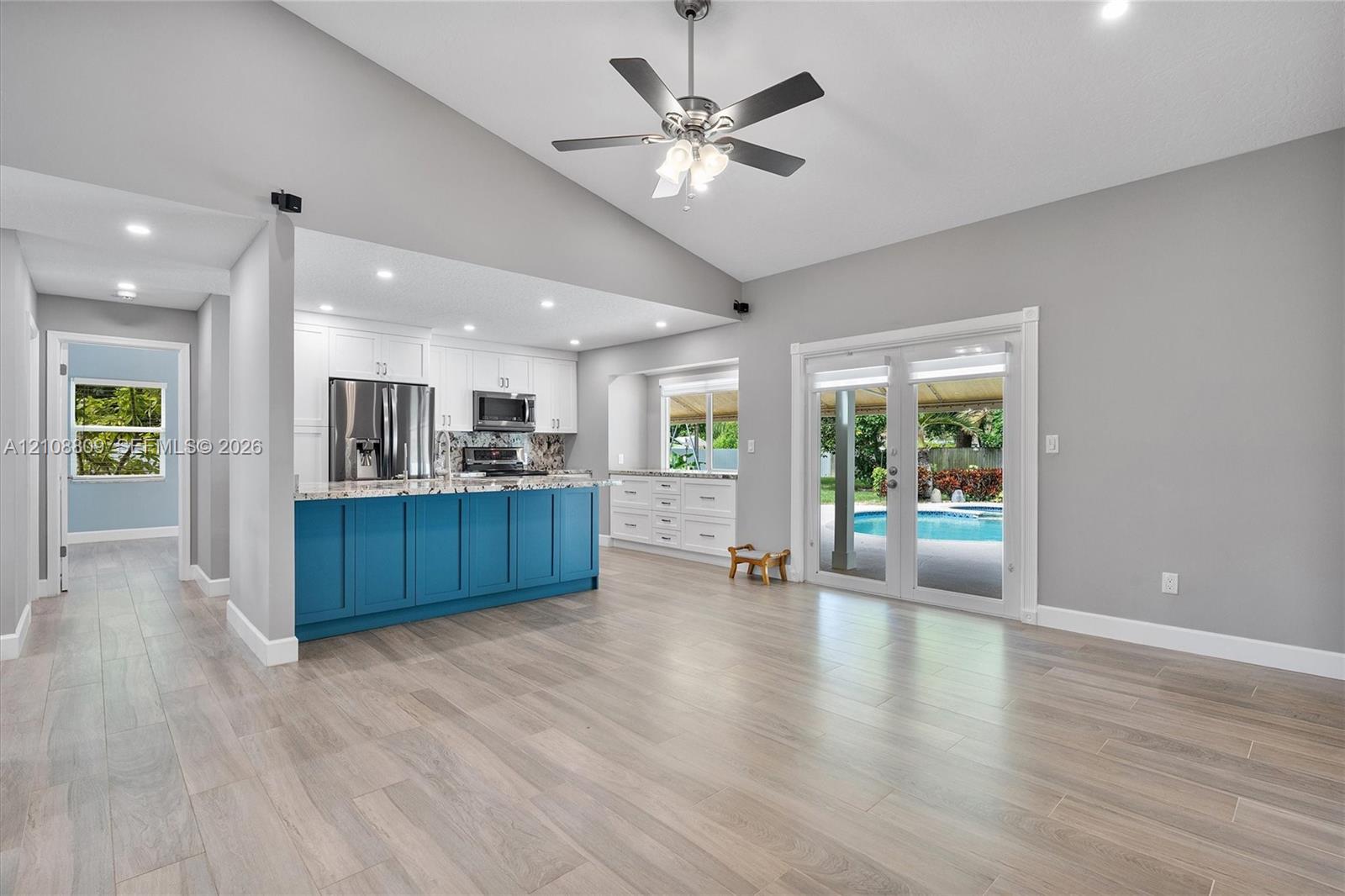 Vaulted ceilings featuring a central ceiling fan, wood-finish flooring, kitchen island with cabinetry, recessed lighting, and double glass-paned doors