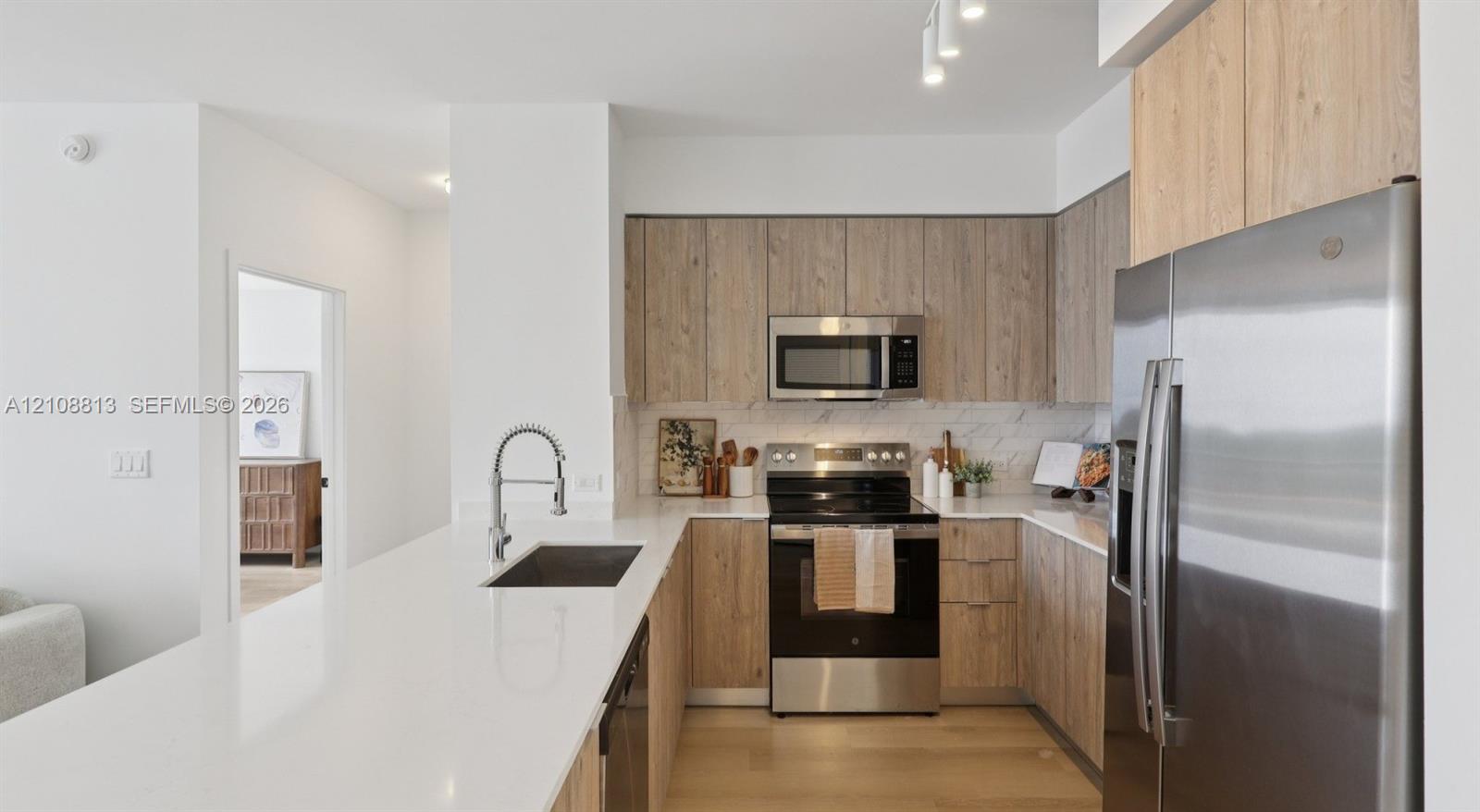 Kitchen featuring wood-finish cabinetry, white solid-surface countertops, stainless steel appliances, and an undermount sink with a pull-down faucet