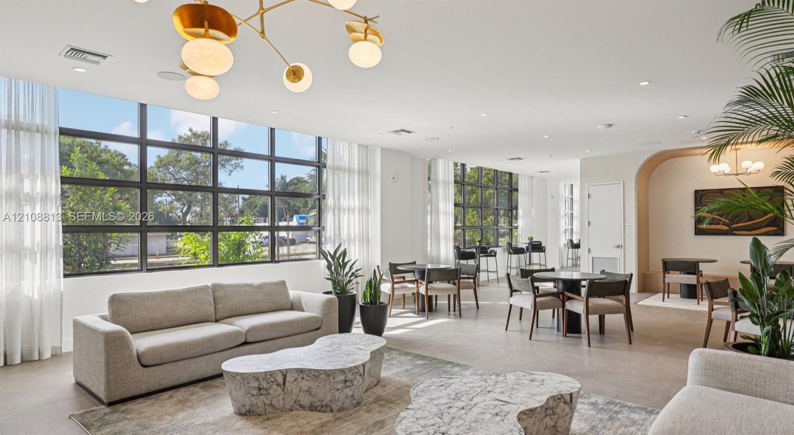 Expansive floor-to-ceiling windows, sculptural multi-arm chandelier, recessed ceiling lighting, porcelain tile flooring, and a curved architectural wall feature
