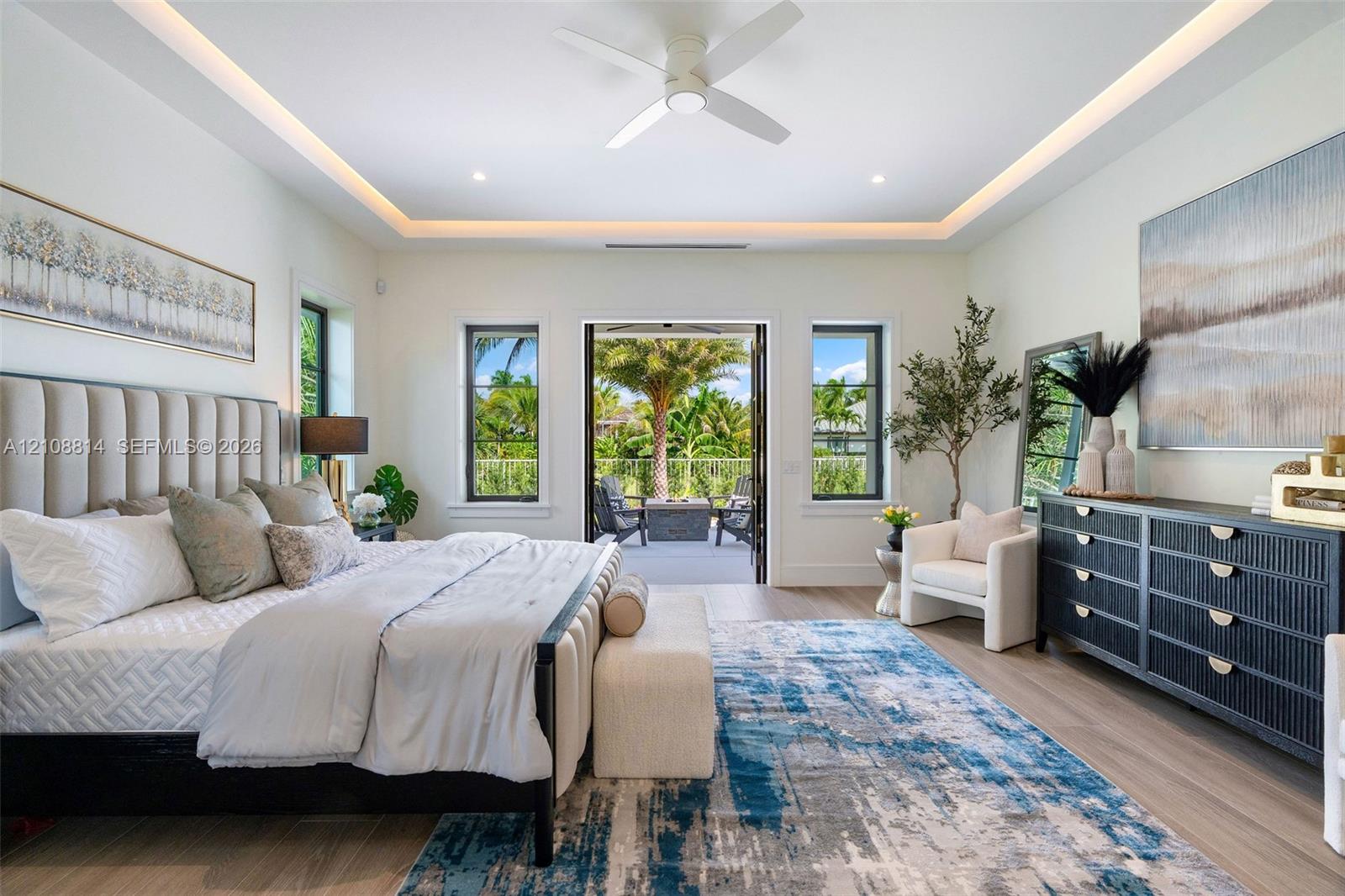 Bedroom featuring a tray ceiling with cove lighting, porcelain-finish flooring, a ceiling fan, and multi-pane windows with glass door access to an exterior area