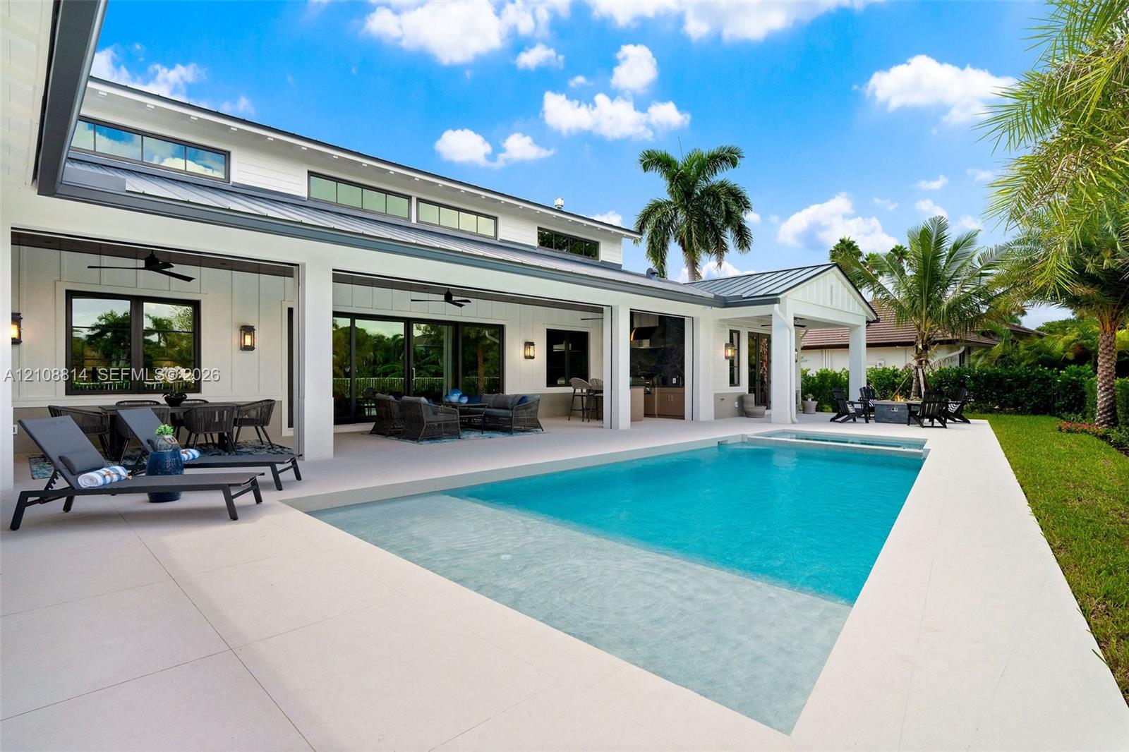 Covered lanai with recessed lighting, in-ground pool featuring a sun shelf, integrated spa, and vertical board-and-batten siding