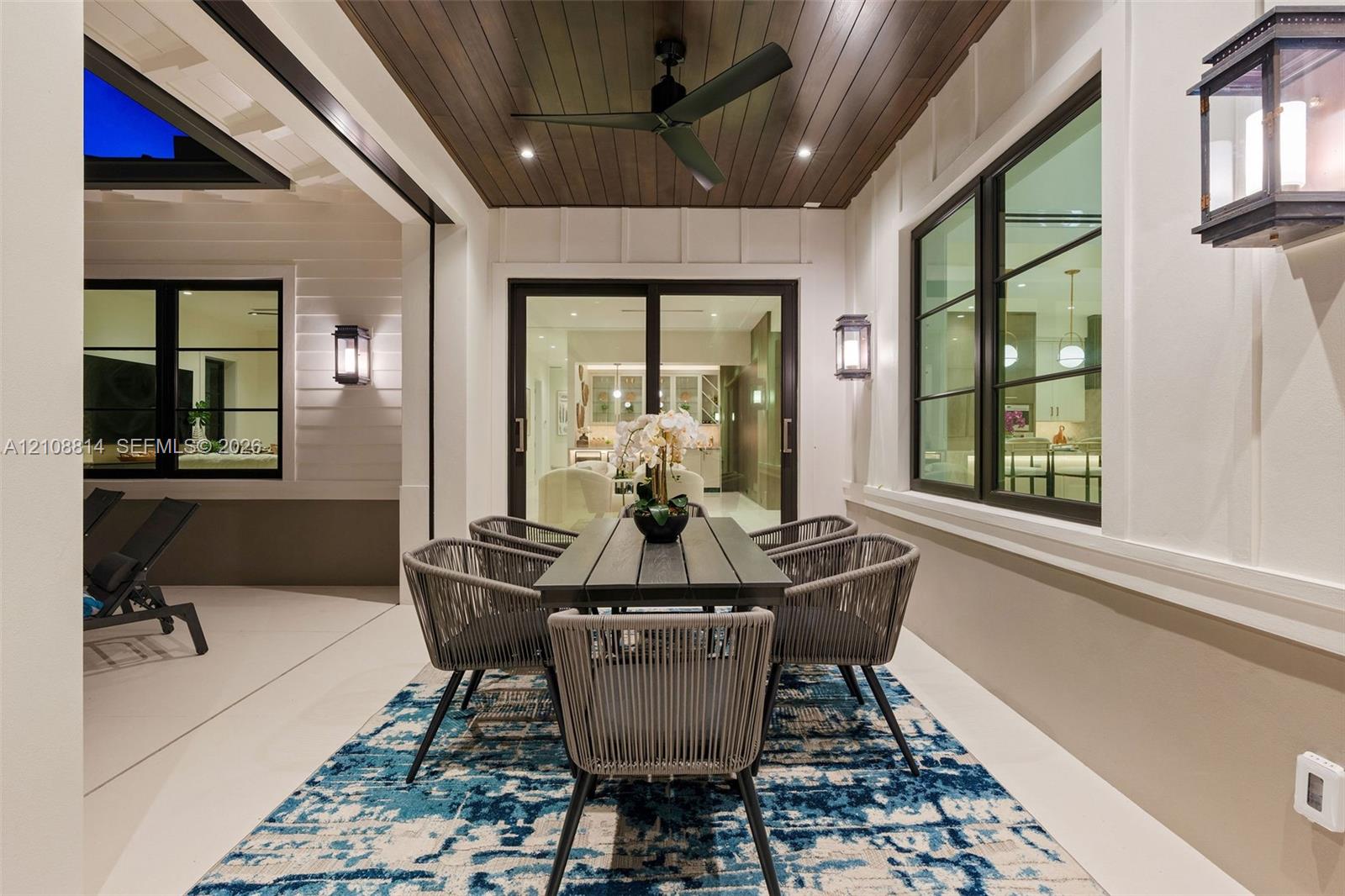 Covered patio featuring a wood-plank ceiling, matte black ceiling fan, recessed lighting, wall-mounted exterior lanterns, and multi-panel sliding glass doors