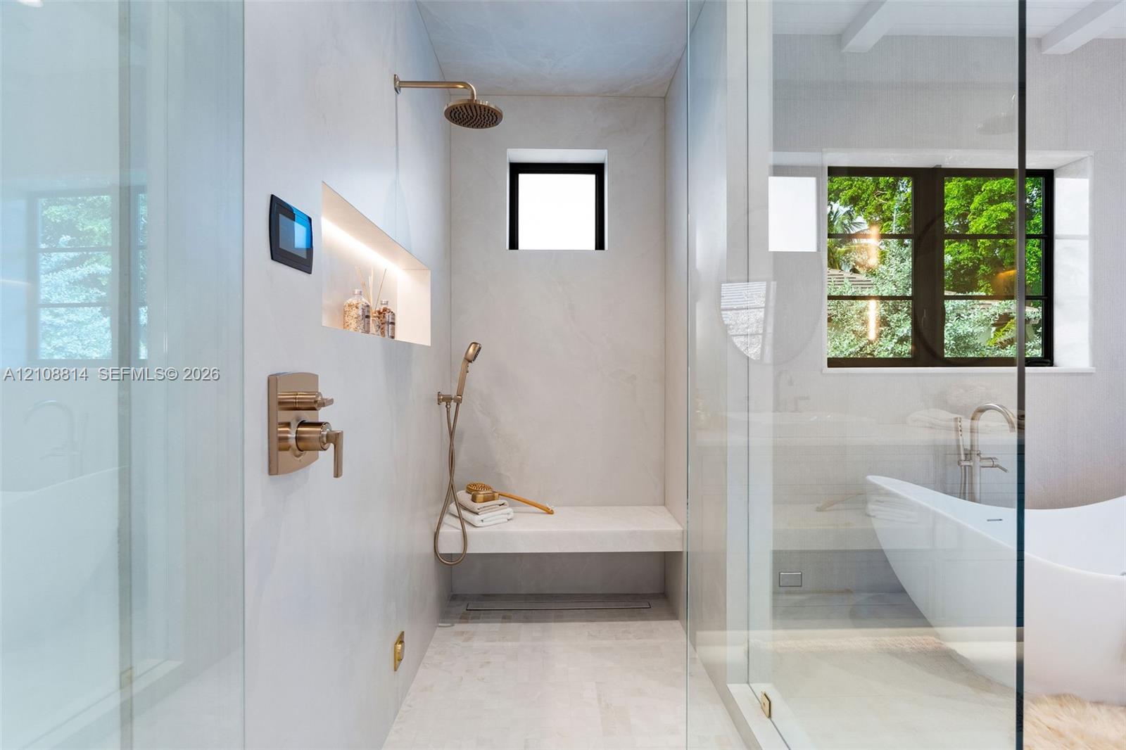 Walk-in shower featuring a built-in stone bench, rain showerhead with handheld sprayer, recessed shelving with integrated lighting, digital control interface, and floor-to-ceiling glass enclosure